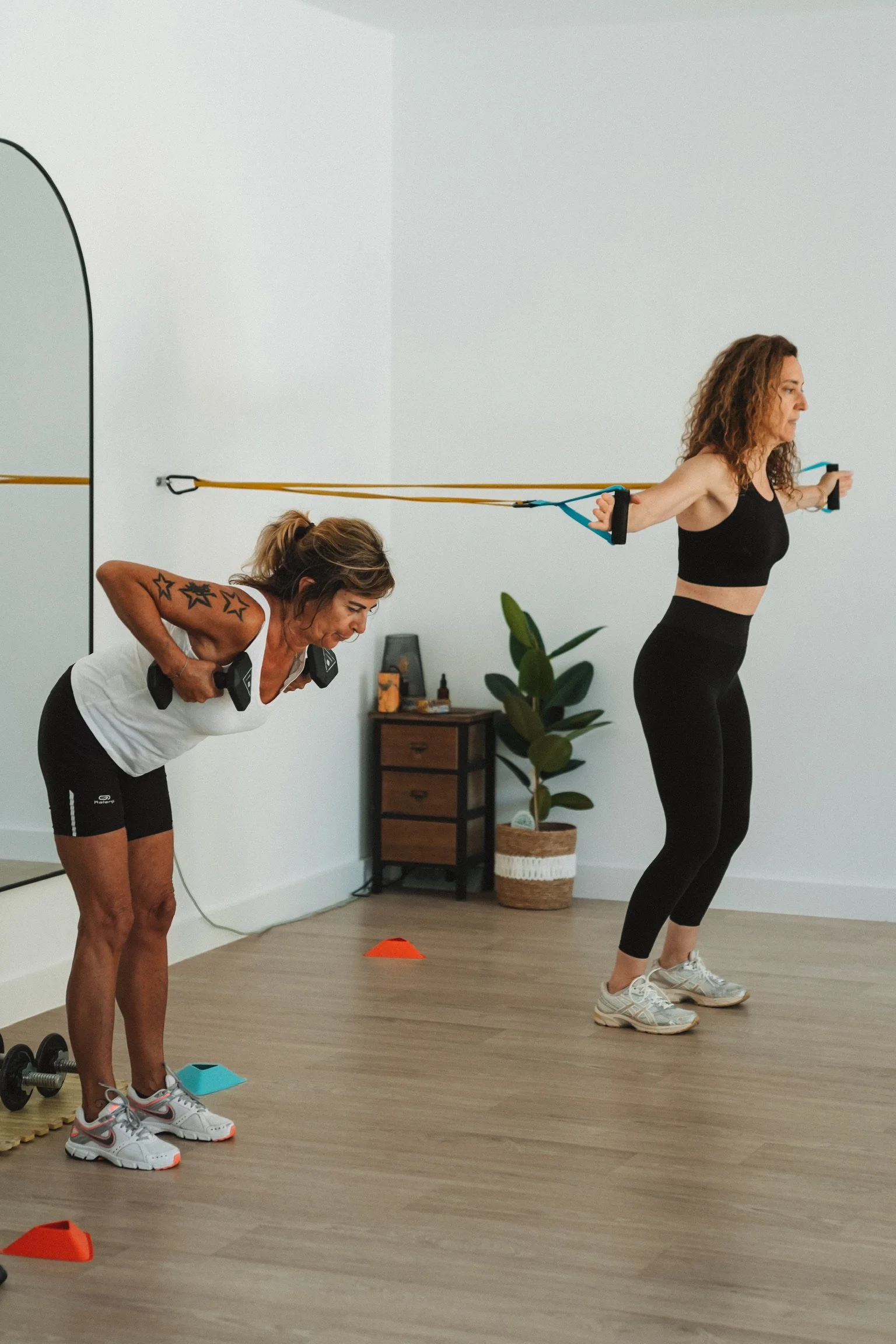 Deux femmes font de l'exercice avec des bandes de résistance dans une salle d'entraînement. La femme à gauche est pliée en avant, la femme à droite tire sur ses bandes avec ses bras tendus en arrière.