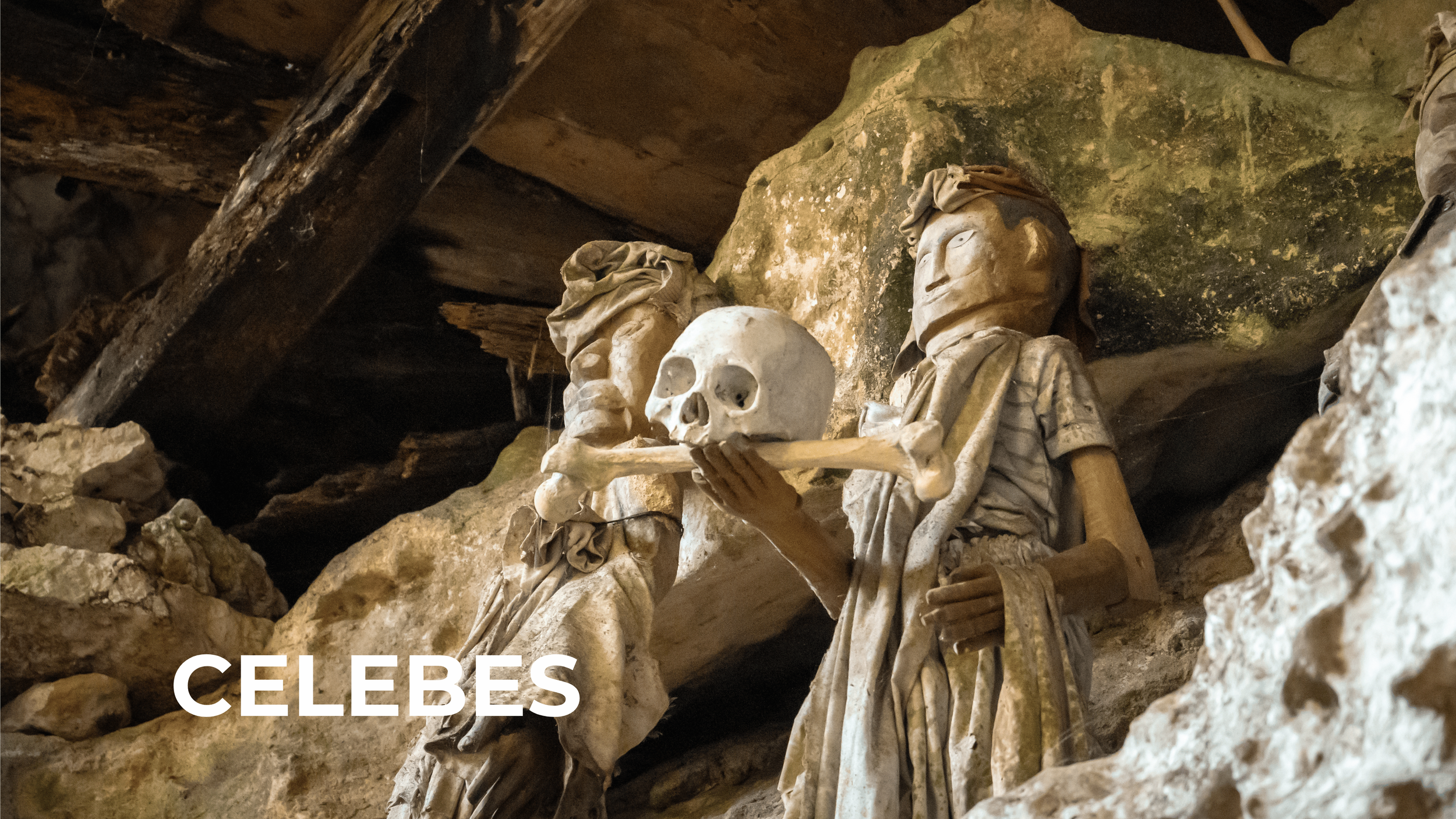 A sculpture of two figures holding a skull, situated in a rocky cave.