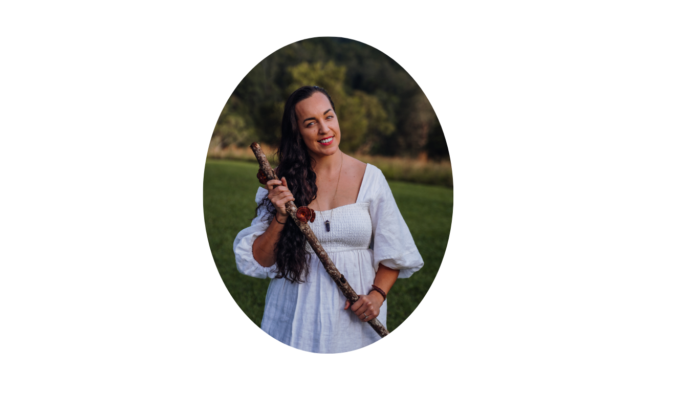 Woman in white dress holding a staff outdoors in a grassy field with trees in the background.