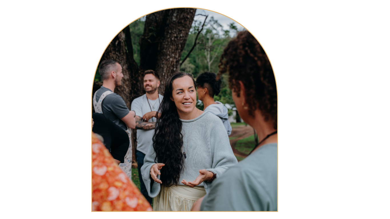 Group of diverse people talking outdoors in a park, with a woman with long dark hair smiling at a woman with curly hair, trees in the background, during daytime.