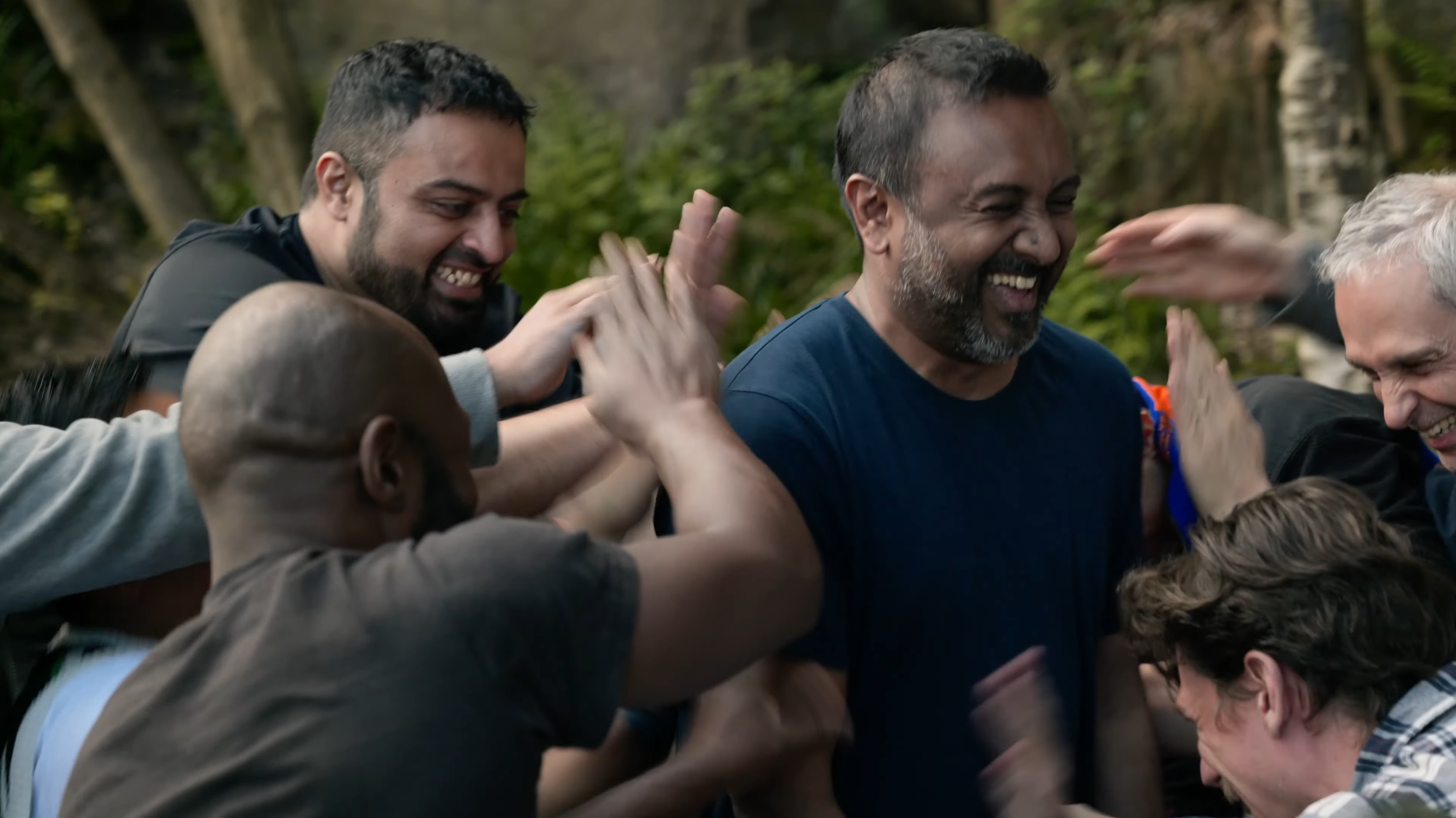 Group of diverse people outdoors smiling and giving high-fives in celebration.