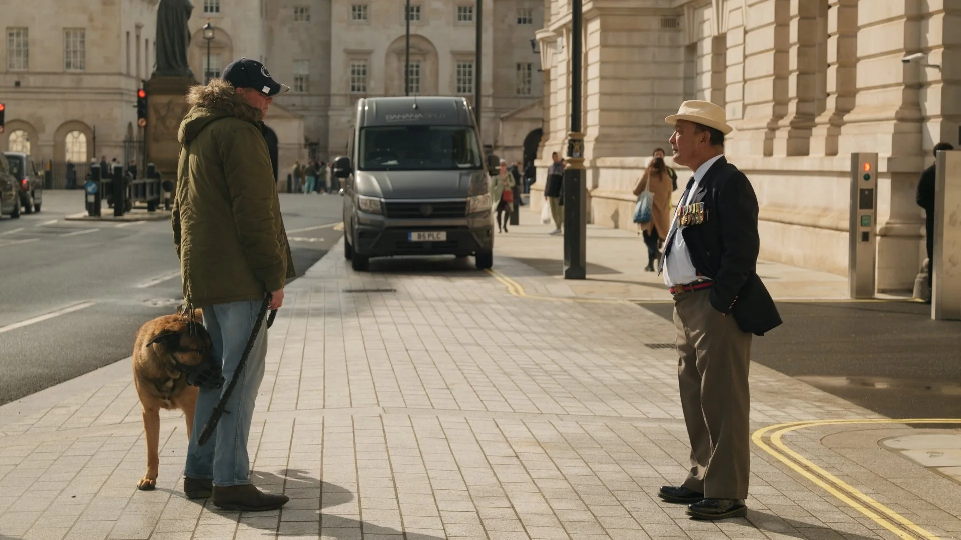 A man with a dog talking to an older man with medals on his blazer on a city sidewalk.