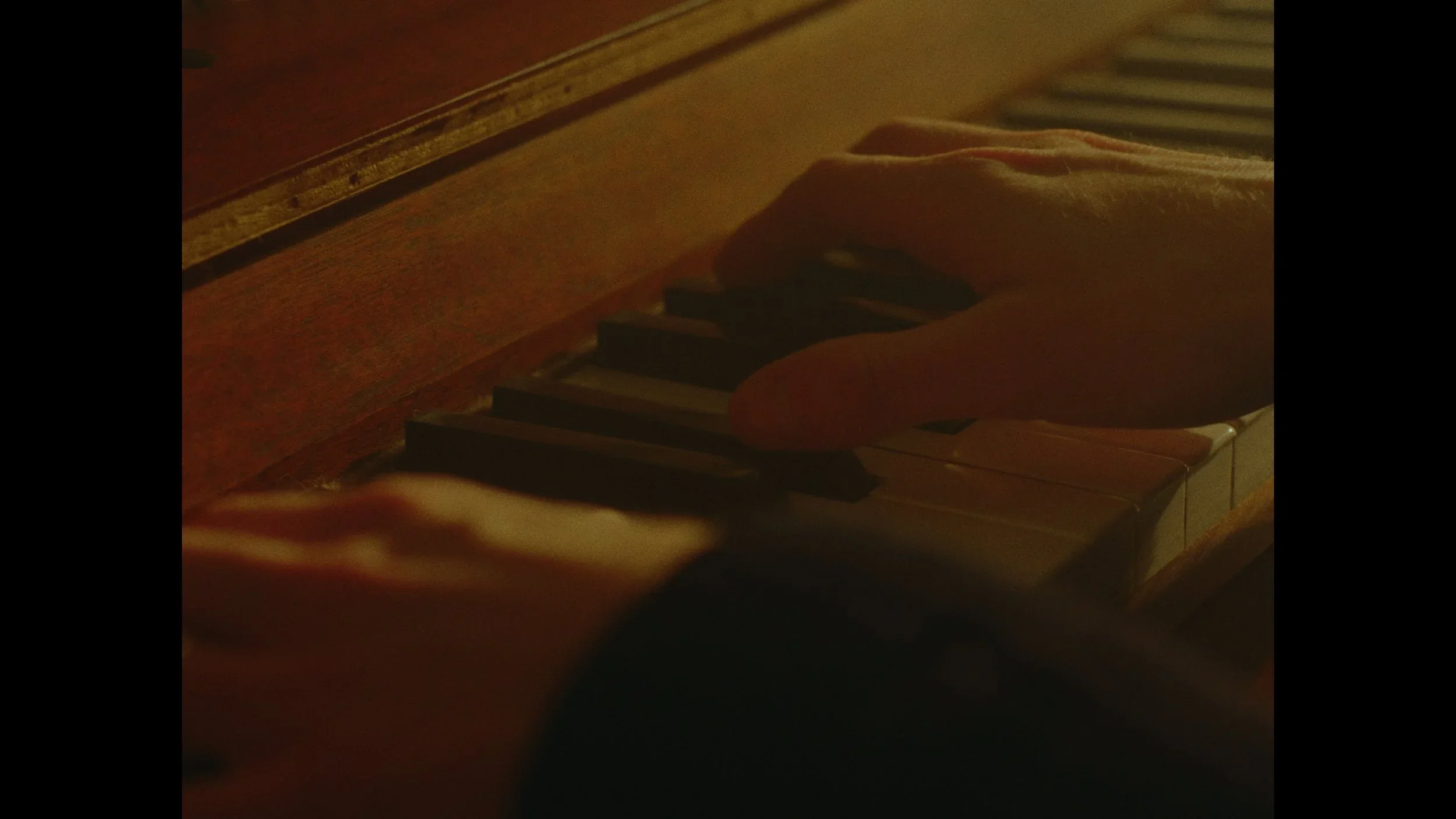 Close-up of a person's hand playing piano keys in dim lighting.
