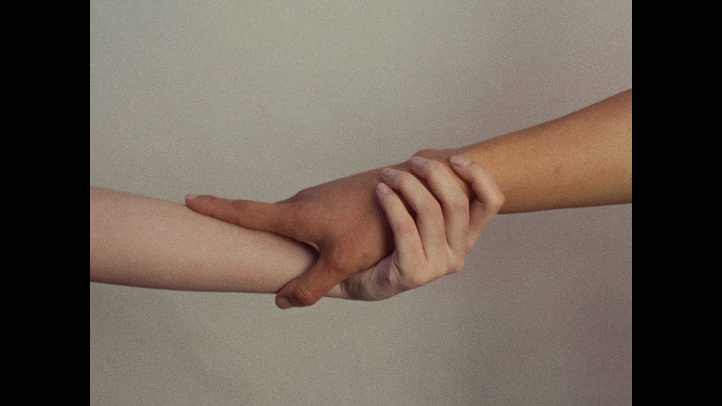Two hands holding each other, one darker-skinned and one lighter-skinned, against a plain light-colored background.