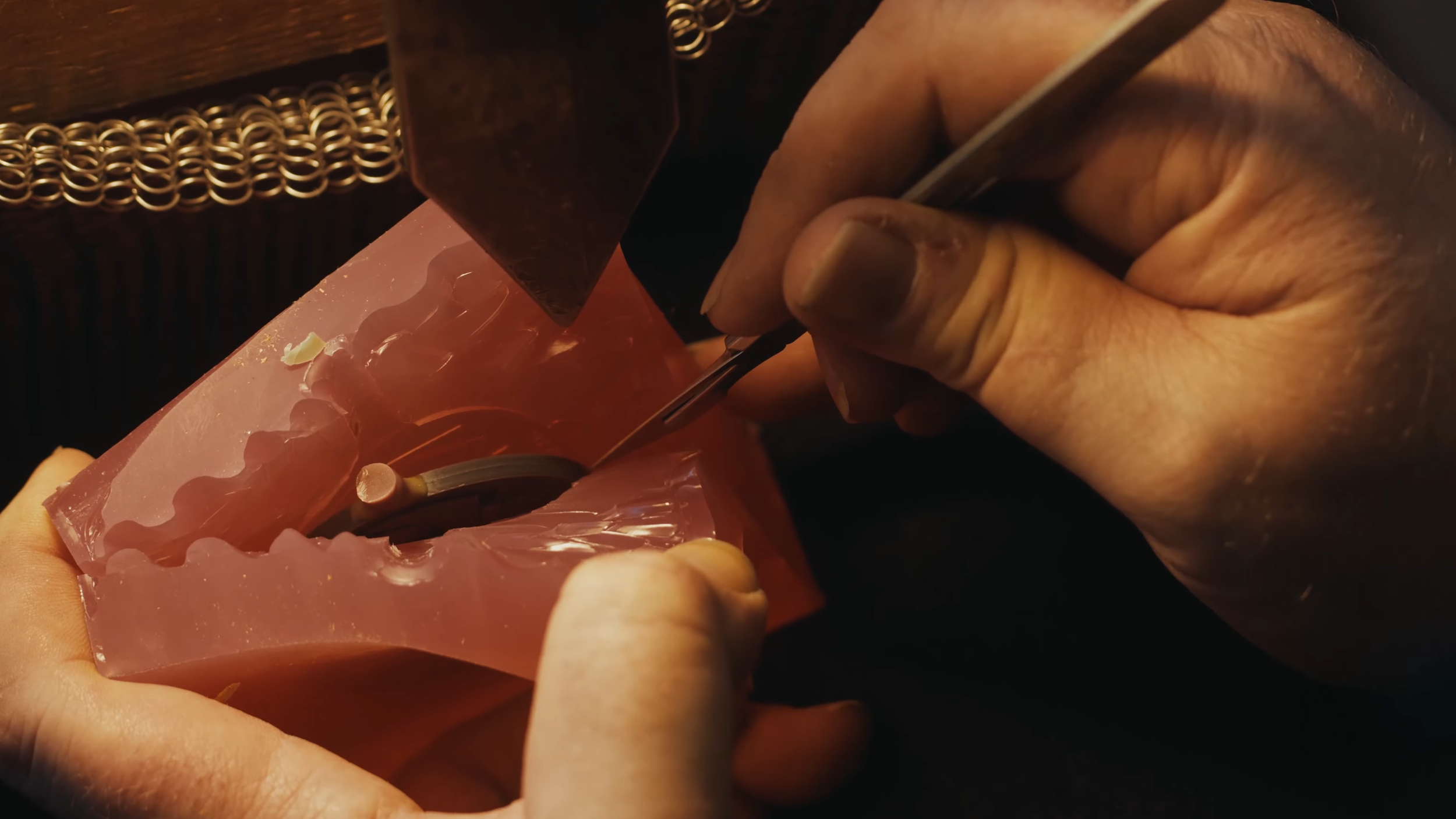 Close-up of a person working on a mechanical component, possibly a watch or a small device, using fine tools in a dark, detailed setting.
