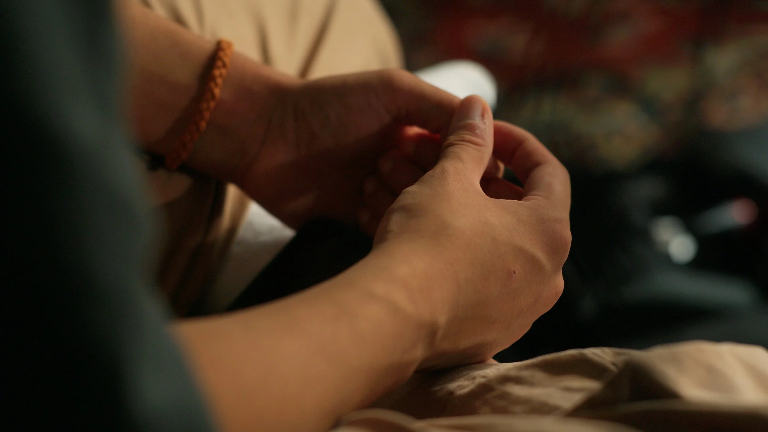 Close-up of two people holding hands, with one person's arm wearing a red woven bracelet.