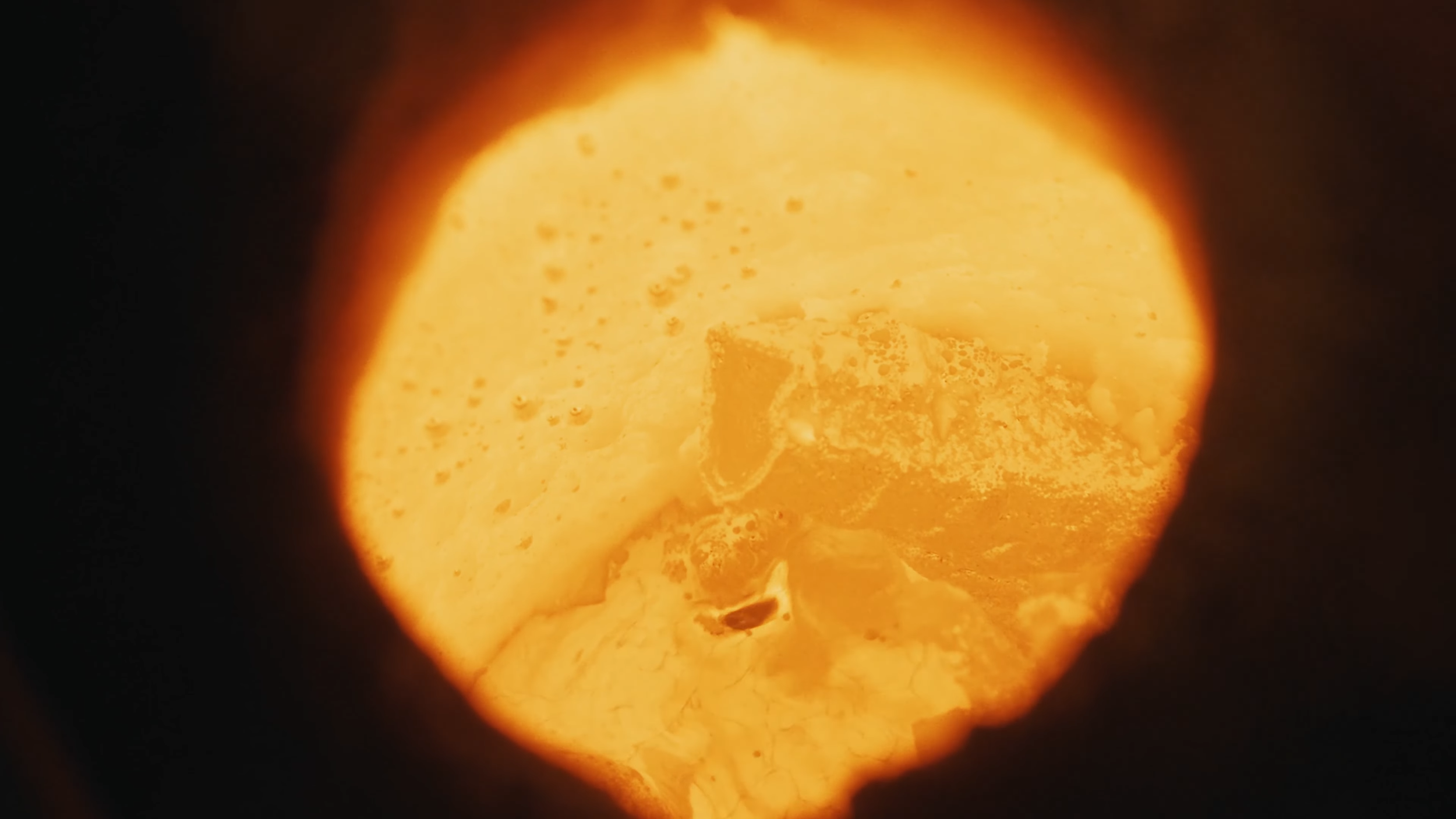 A close-up view of a block of yellow cheese with holes, viewed through a circular opening.