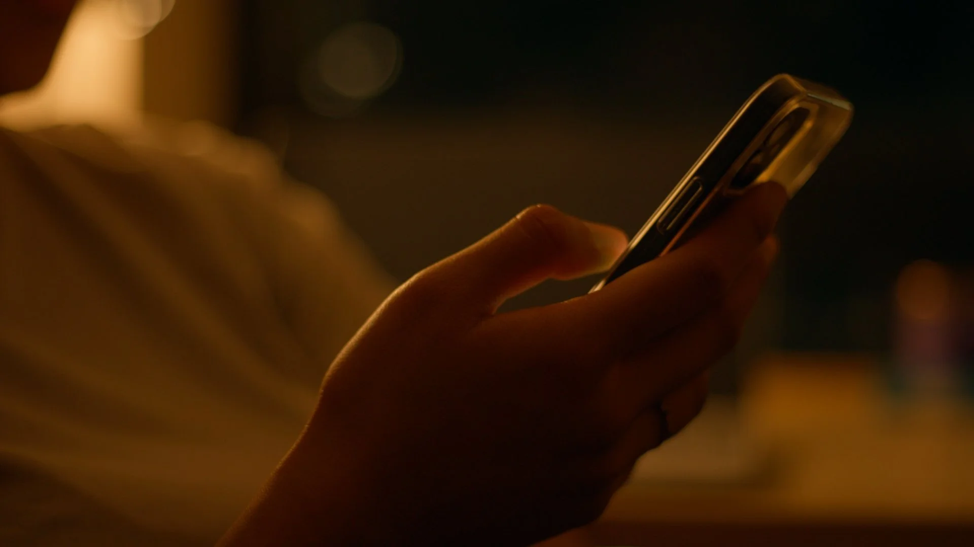 Close-up of a hand holding a smartphone in a dimly lit environment.