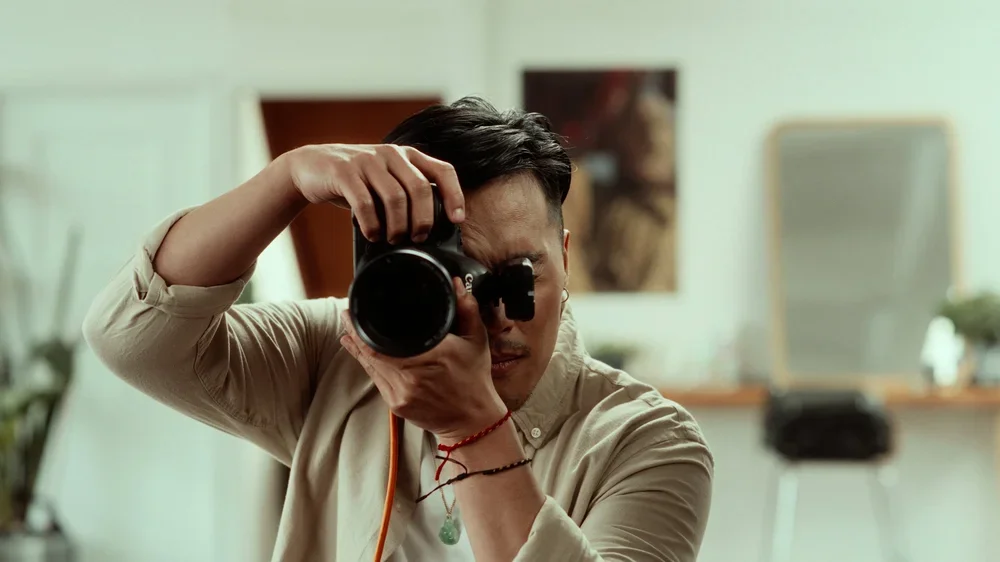 A man taking a picture of himself with a camera in a room with mirrors and artwork.