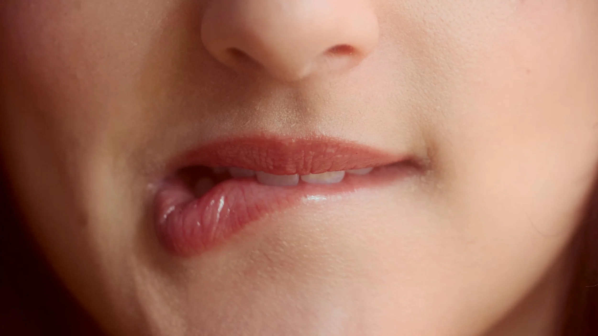 Close-up of a person's partially open lips with pink lipstick, showing teeth and a finger touching the lower lip.