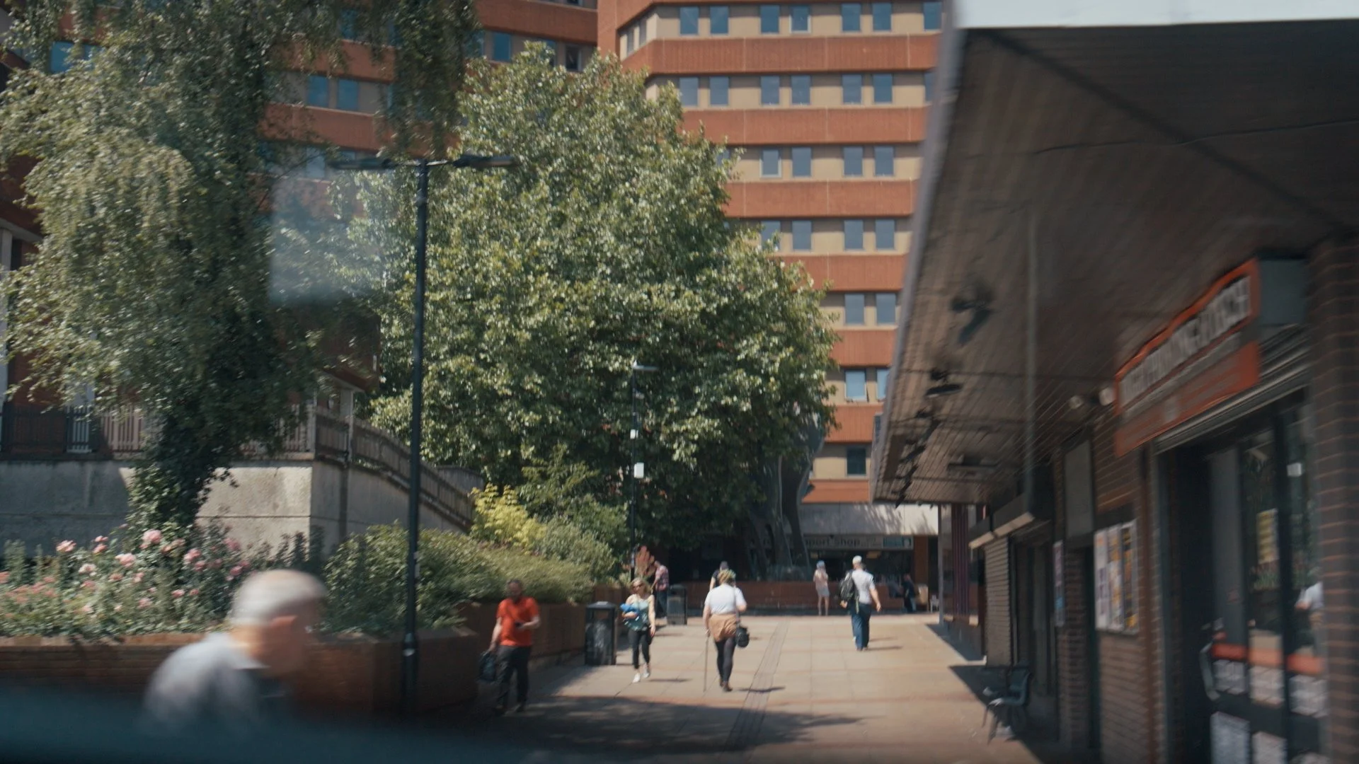 City sidewalk with pedestrians, a tall building, and trees, with a business storefront on the right with a sign that reads 'Smart Shop'.