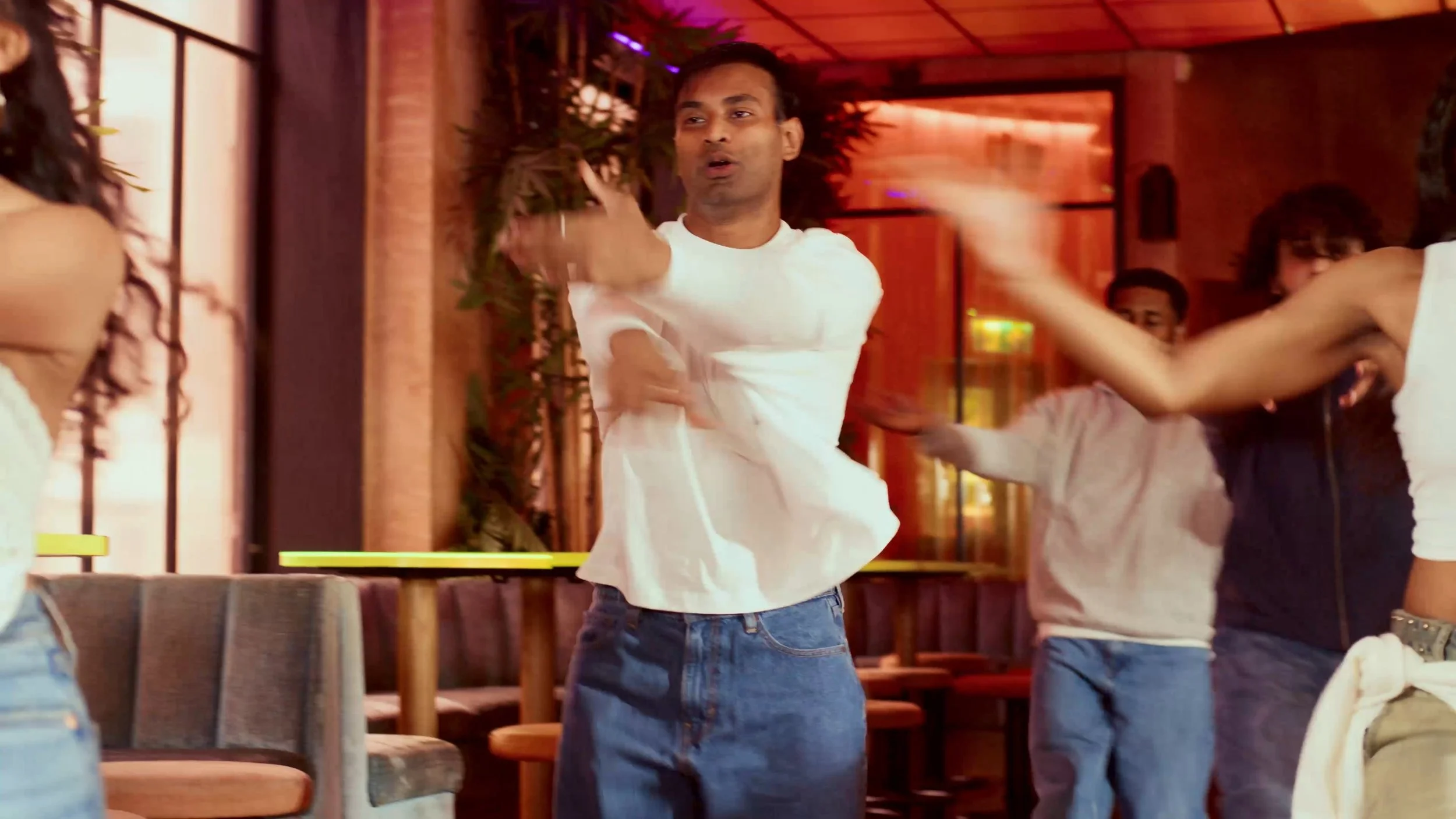 Man dancing with young girls in a warmly lit indoor space, likely a restaurant or café.