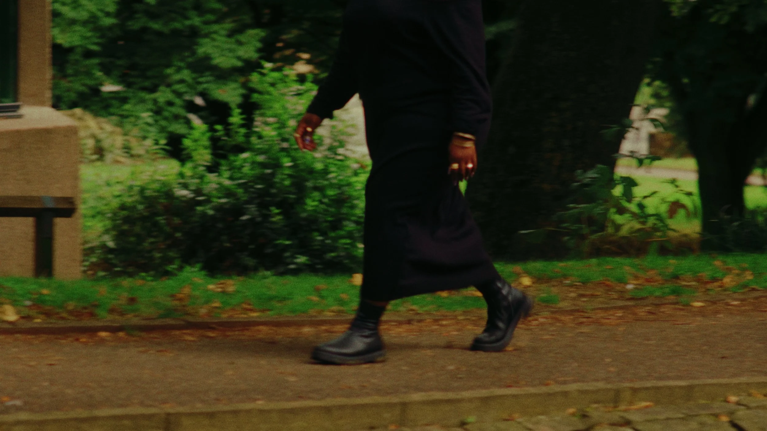 Person walking on a sidewalk in a park area with trees and grass.