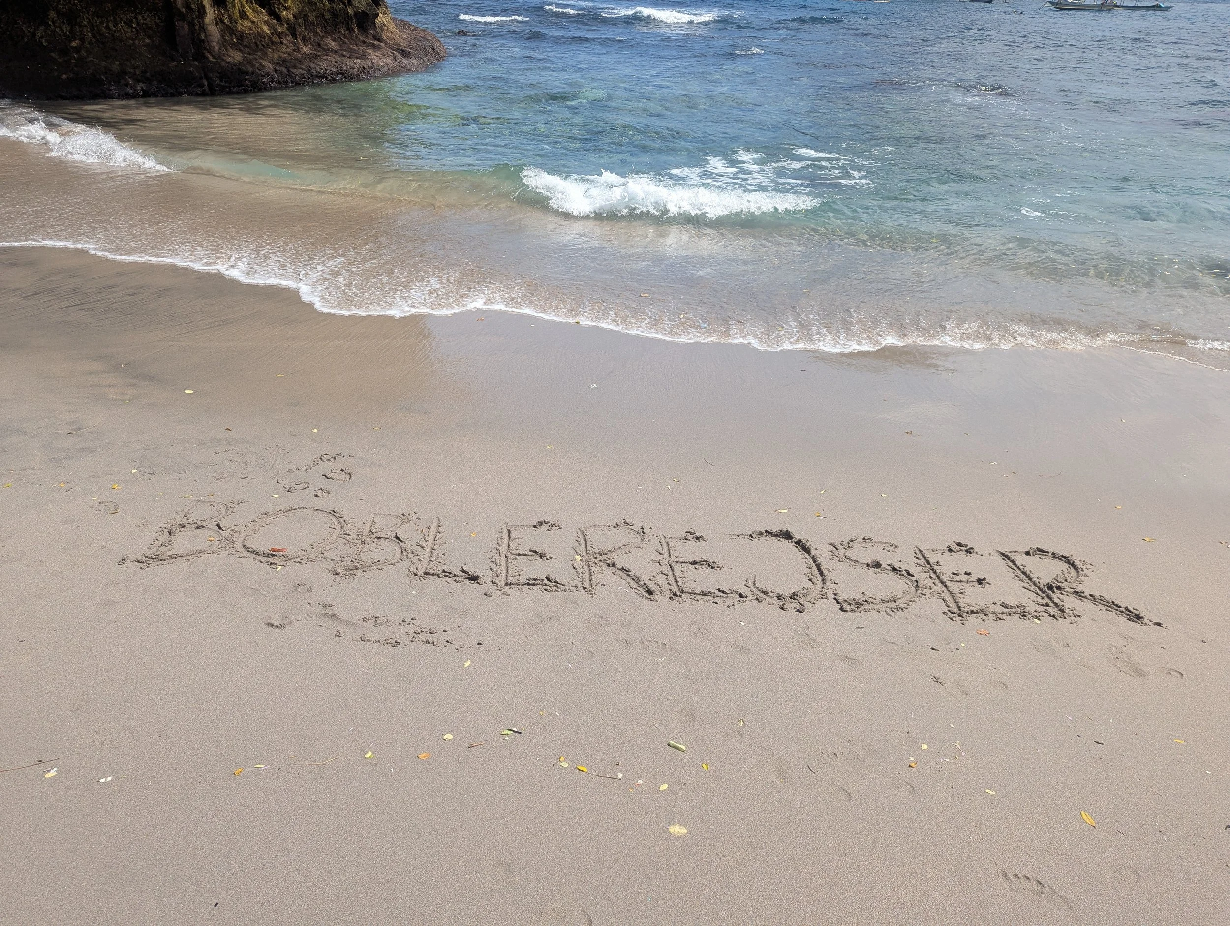 På stranden tæt på Bali, er der skrevet Boblerejser i sandet
