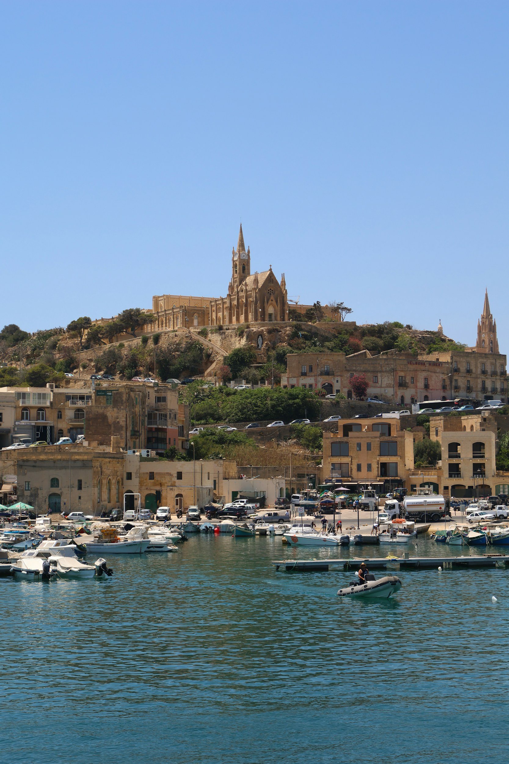 Udsigt over Mgarr havn på Gozo, Malta – både i det klare middelhavsvand og den ikoniske kirke på bakken, et stemningsfuldt syn for rejsende.