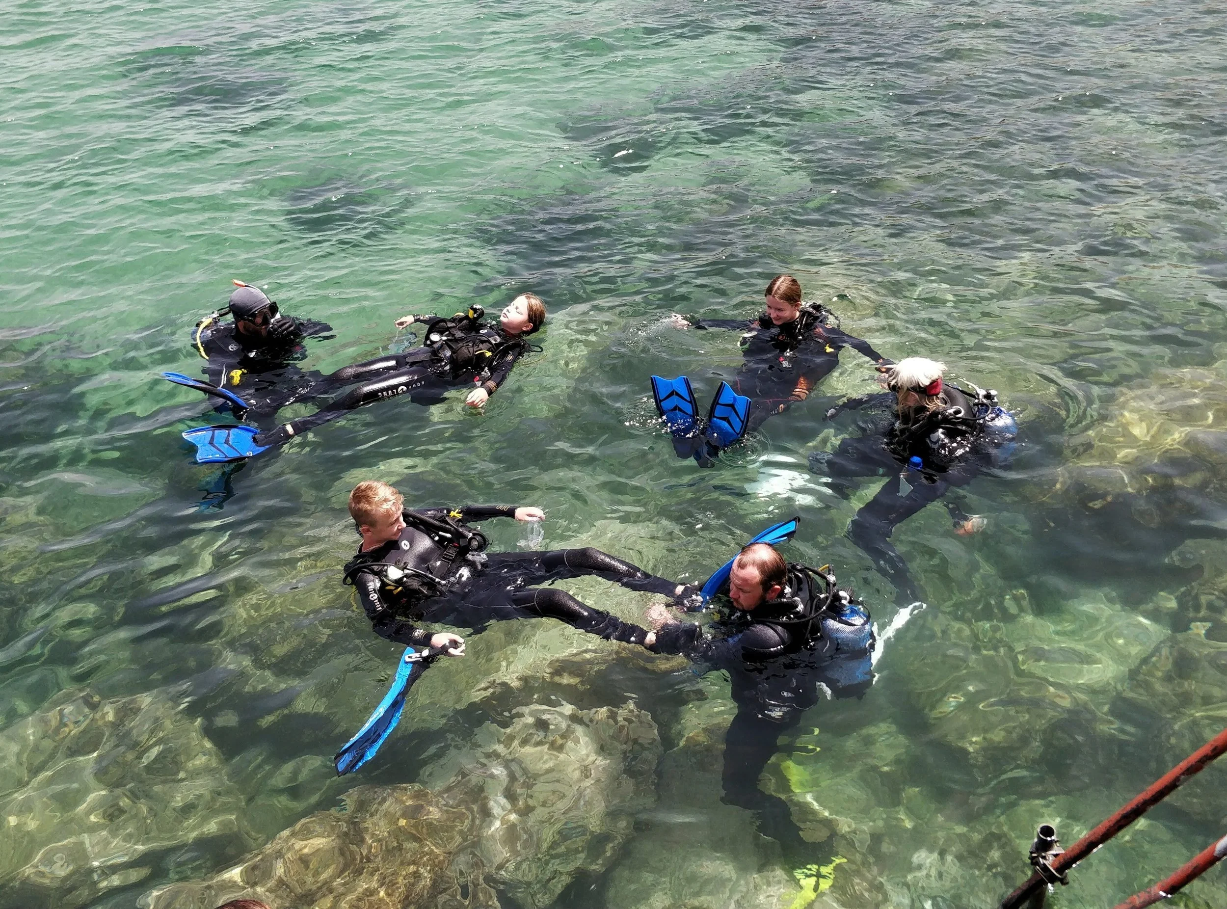Dykkertræning i vand med fire personer udstyret med scuba-udstyr, de flyder alle i vandet og hjælper hinanden med at få det sidste udstyr såsom finner på, inden de skal dykke.