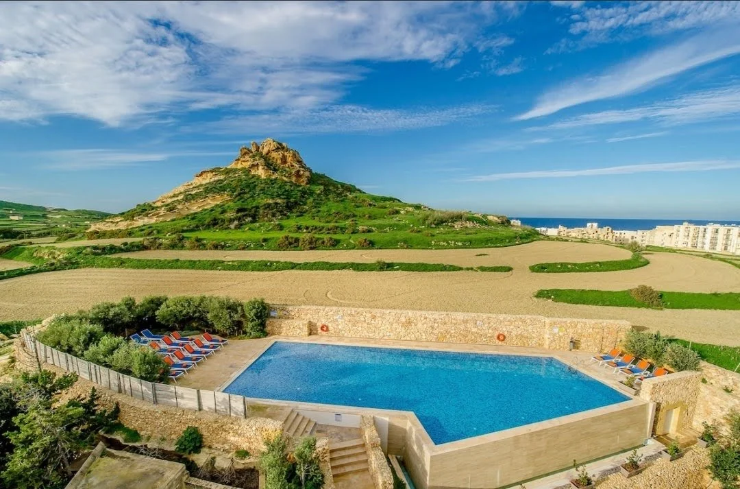 Udsigt over Gozo med pool, solstole og grønne marker – rolig middelhavsstemning og familievenlig ferie med Boblerejser.