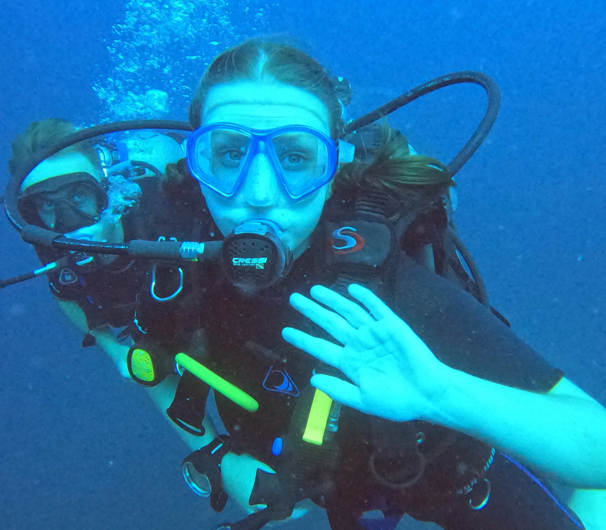 To mennesker dykker under vandet, en af dem nærmest kameraet med en dykkermaske og regulator, begge iført dykkerudstyr.