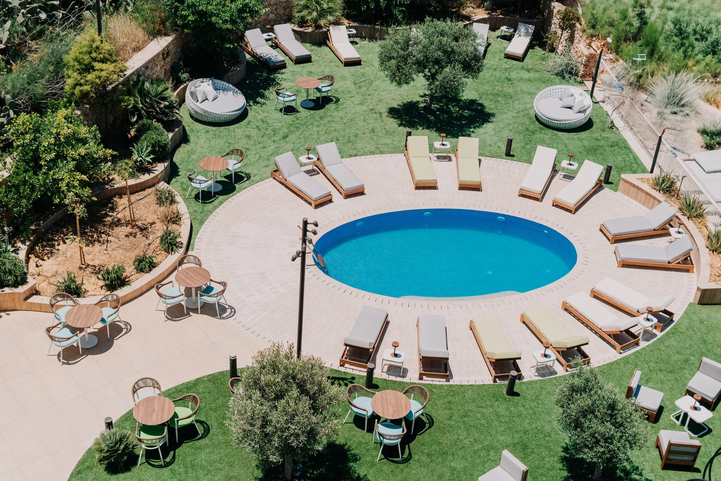 Poolområde med grøn have solstole og borde med parasoller står ved hotel på Gozo (Malta)