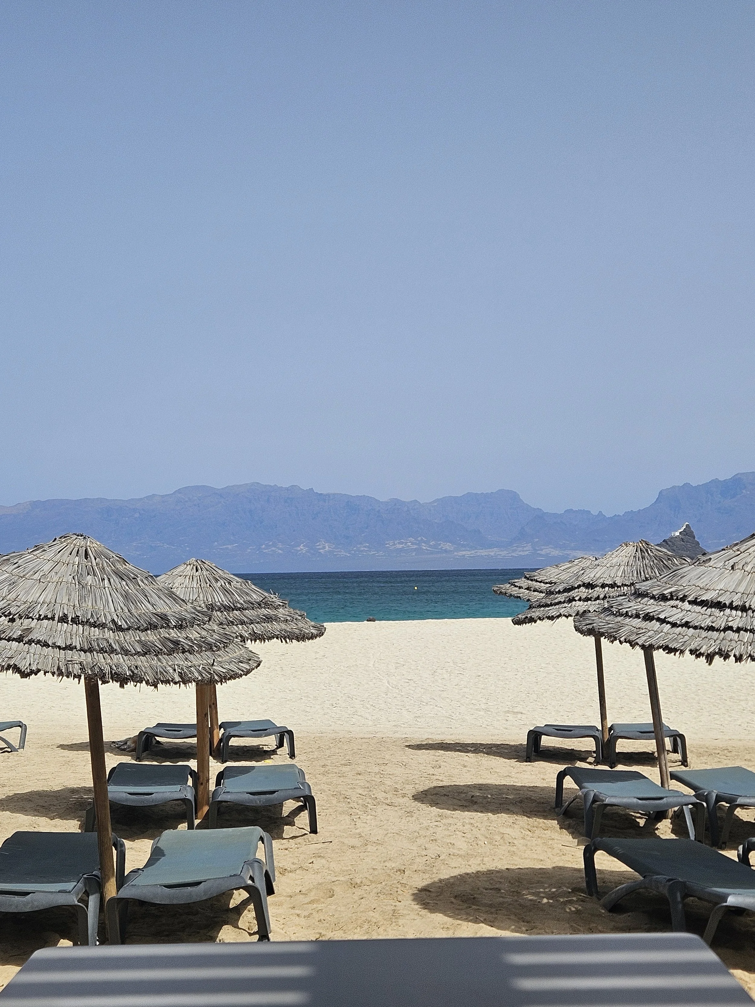 Strand i Mindelo med solstole, parasoller, havet og bjerge som baggrund