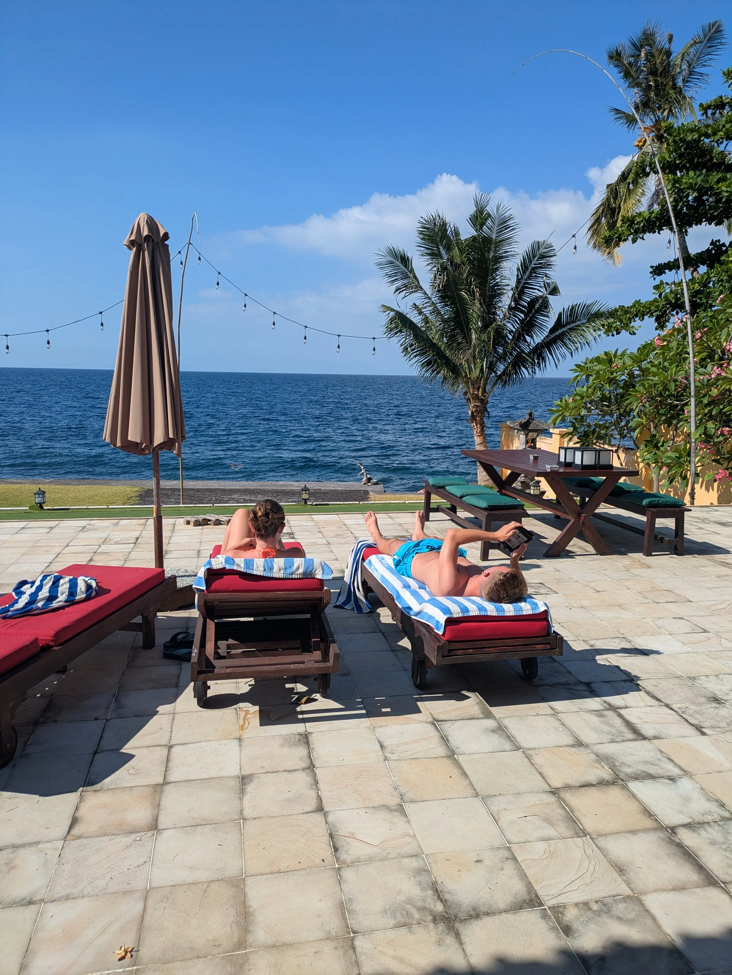To ligger på solsenge og ser over havet på resort på Bali