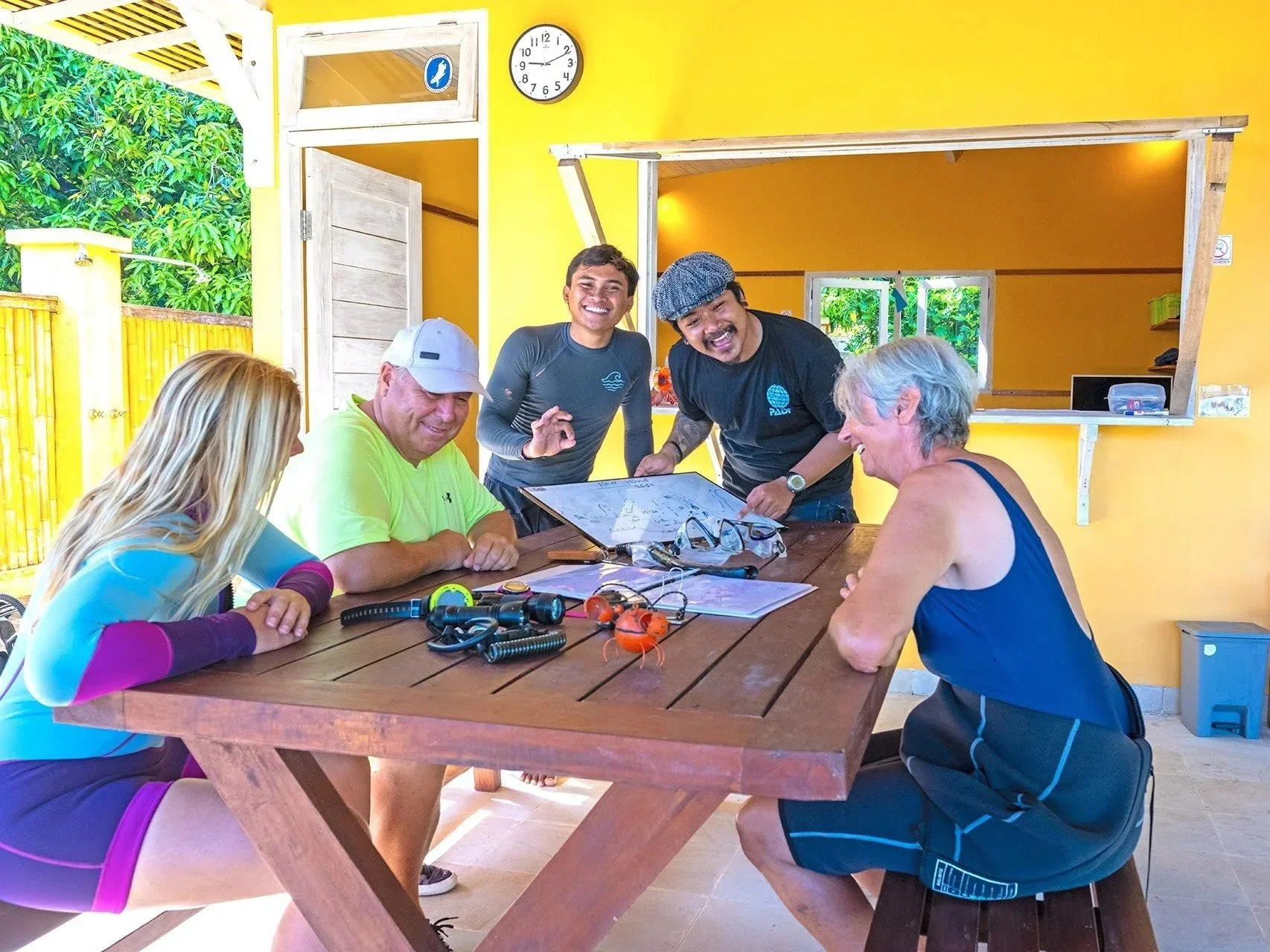 Dykkerinstruktør gennemgår dagens dyk med en familie på Bali – planlægning, grin og fælles forventningsglæde før turen under havet med Boblerejser.
