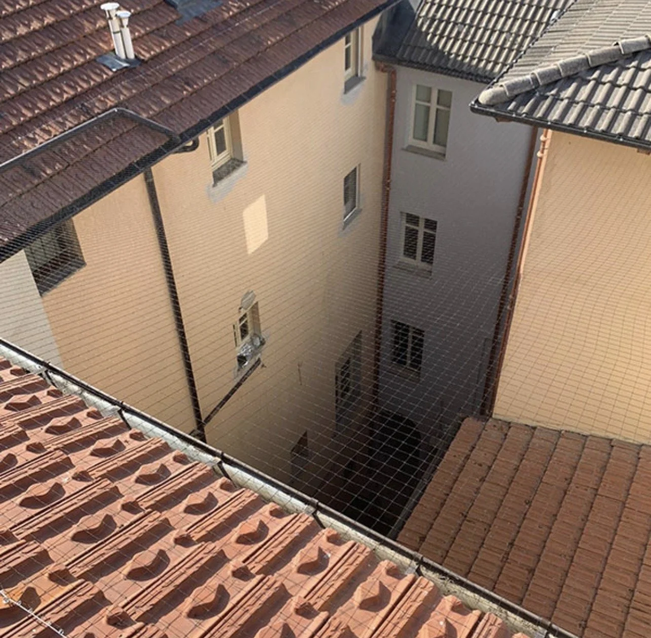 Vista di un cortile tra edifici con tetti di tegole e una rete di sicurezza di metallo.