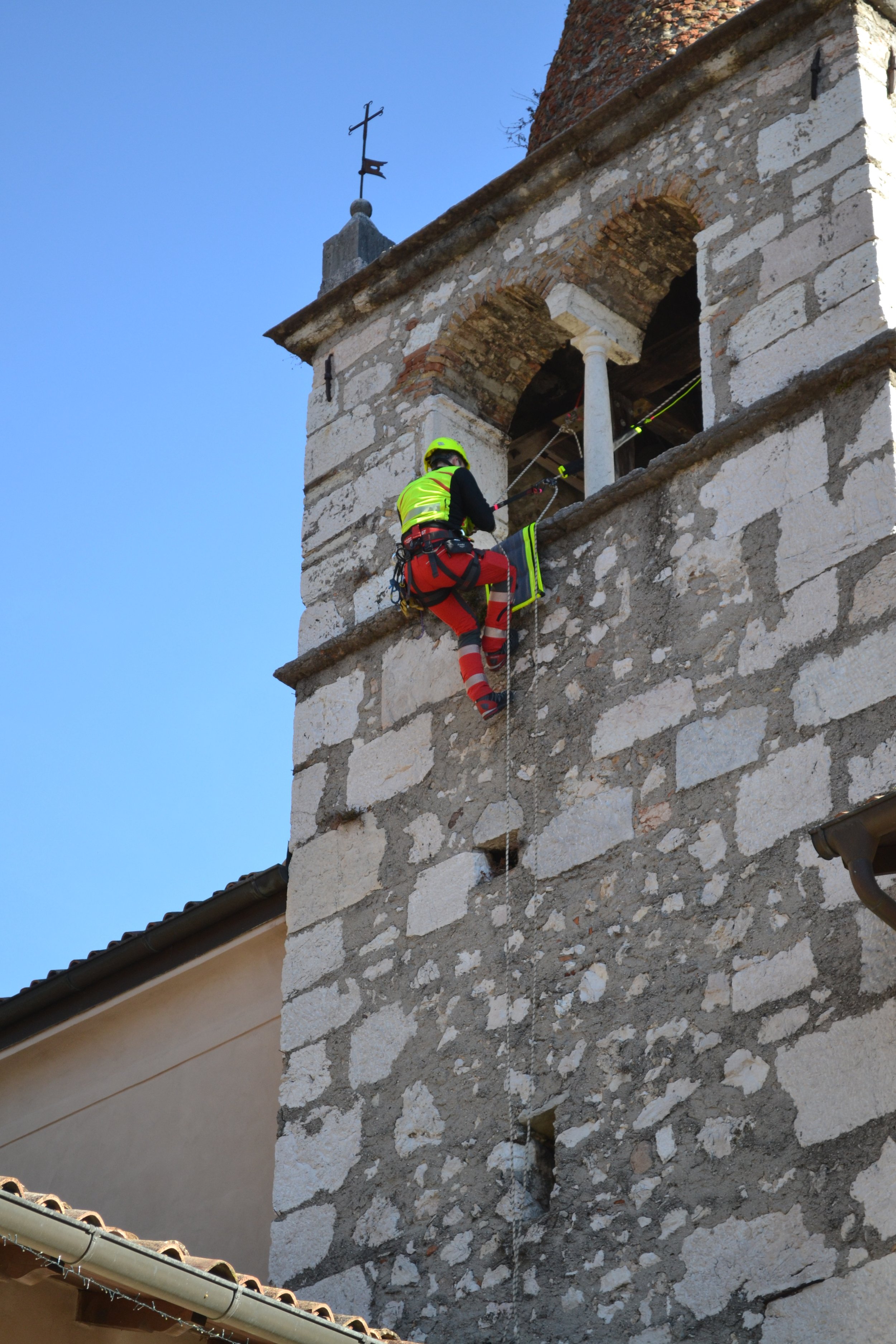 Un operatore sta lavorando sulla torre di un edificio storico, indossando equipaggiamento di sicurezza e una tuta ad alta visibilità.