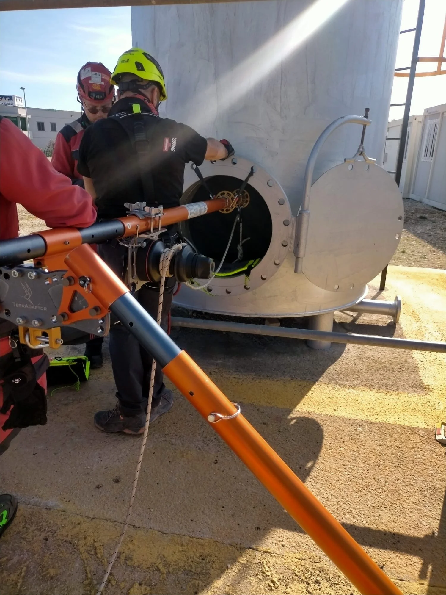 Tre persone in tuta da lavoro e casco stanno eseguendo attività di manutenzione o test su un grande serbatoio metalllico.