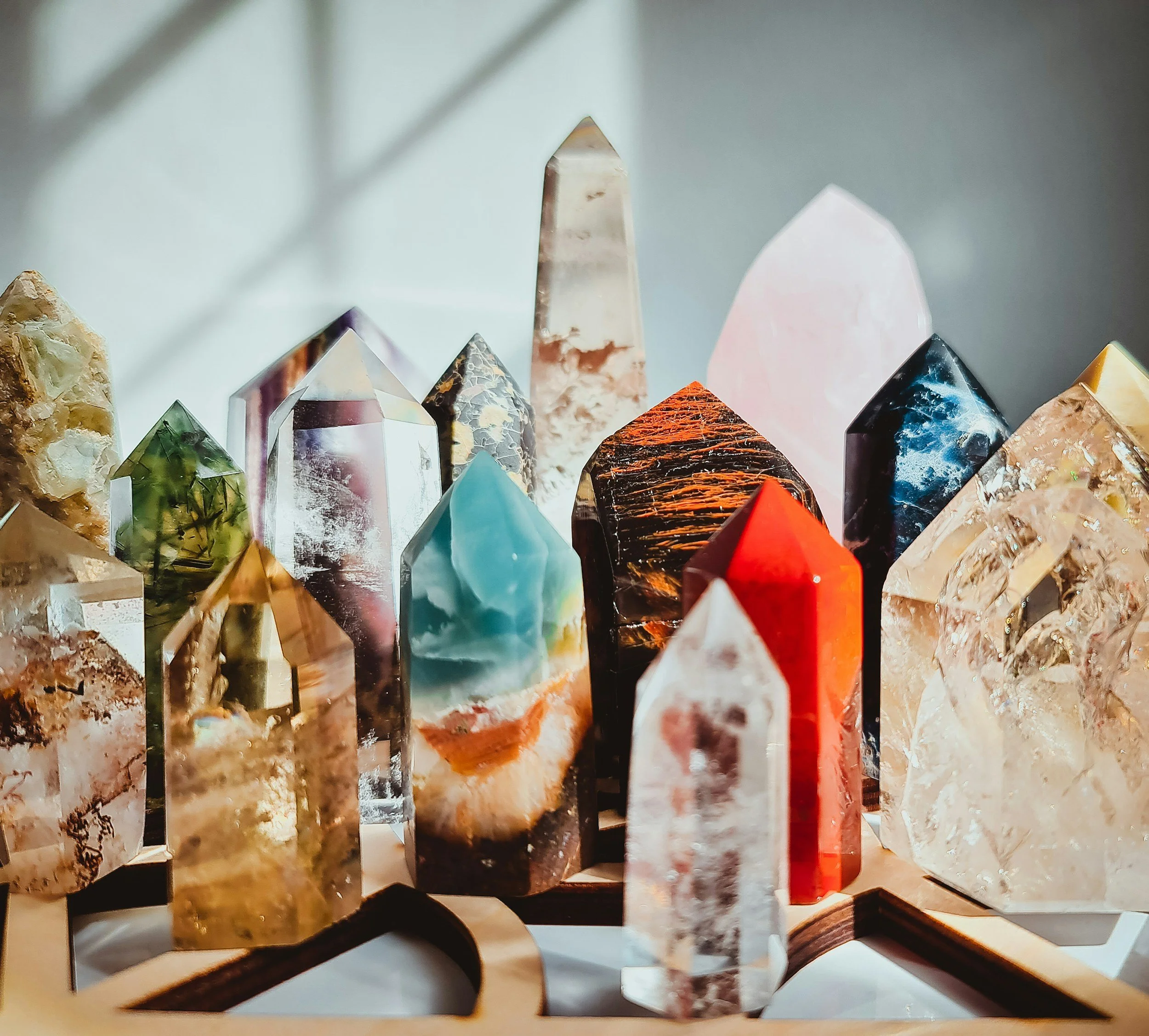 Collection of colorful polished and raw gemstones arranged on a wooden display stand with light and shadow creating a soft background.