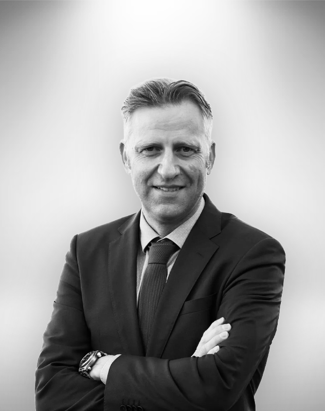 Tomi Tuomisalo henkilökuva, pukeutunut tummaan pukuun ja kravaattin, hymyilee.