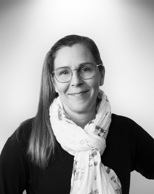 Kristiina Paananen henkilökuva, pukeutuneena mustaan paitaan ja valkoiseen huiviin, hymyilee.
