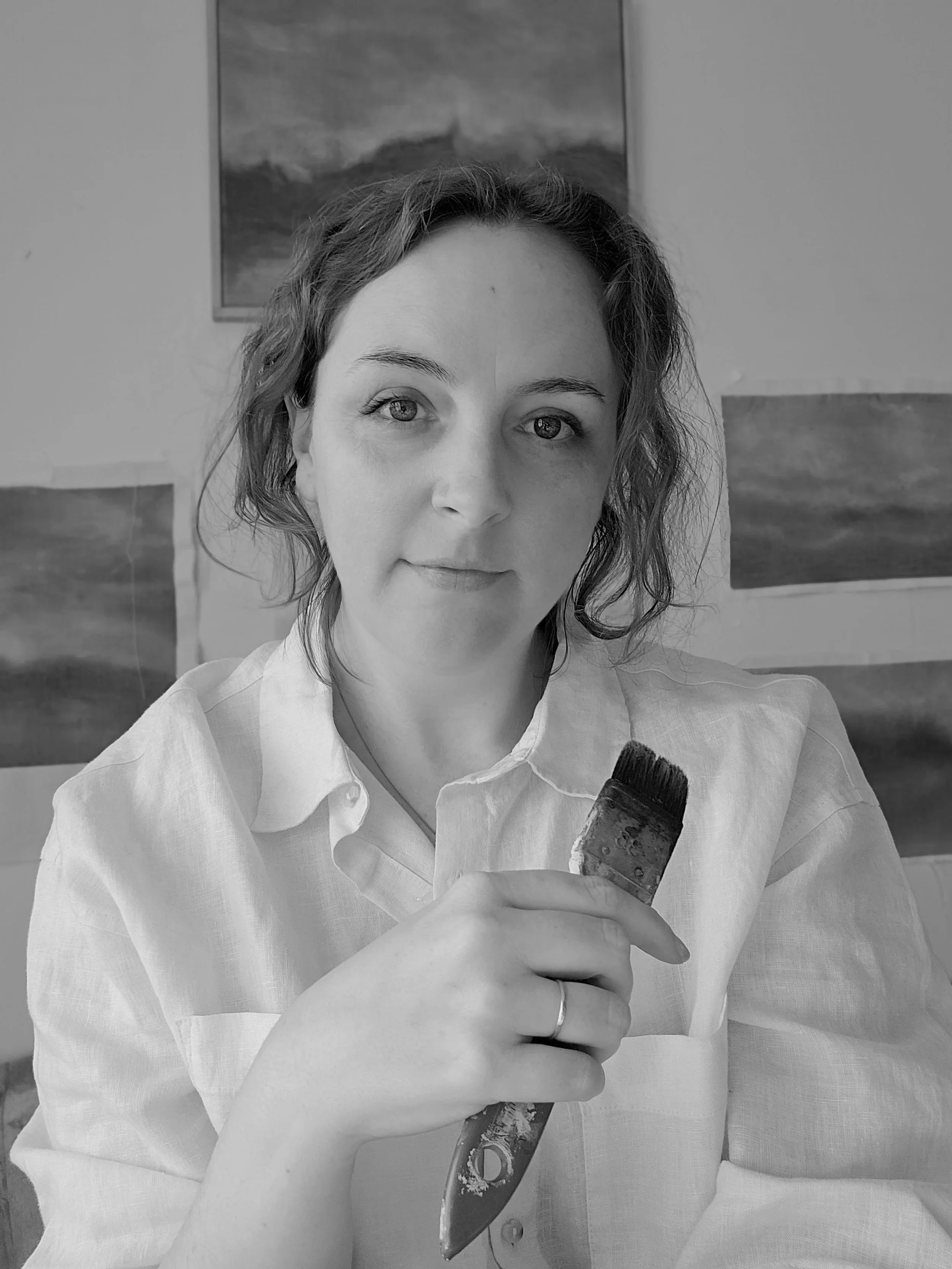 artist posing in front of paintings with paintbrush in hand