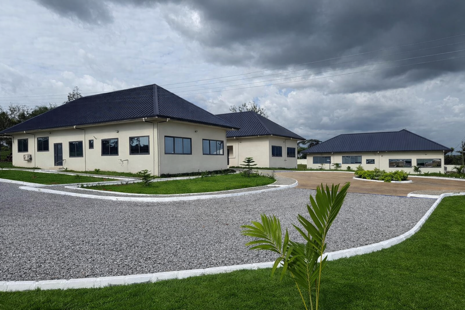 Luxurious modern white houses with dark blue metal roofs surrounded by well-maintained green lawns and landscaped gardens under a cloudy sky.