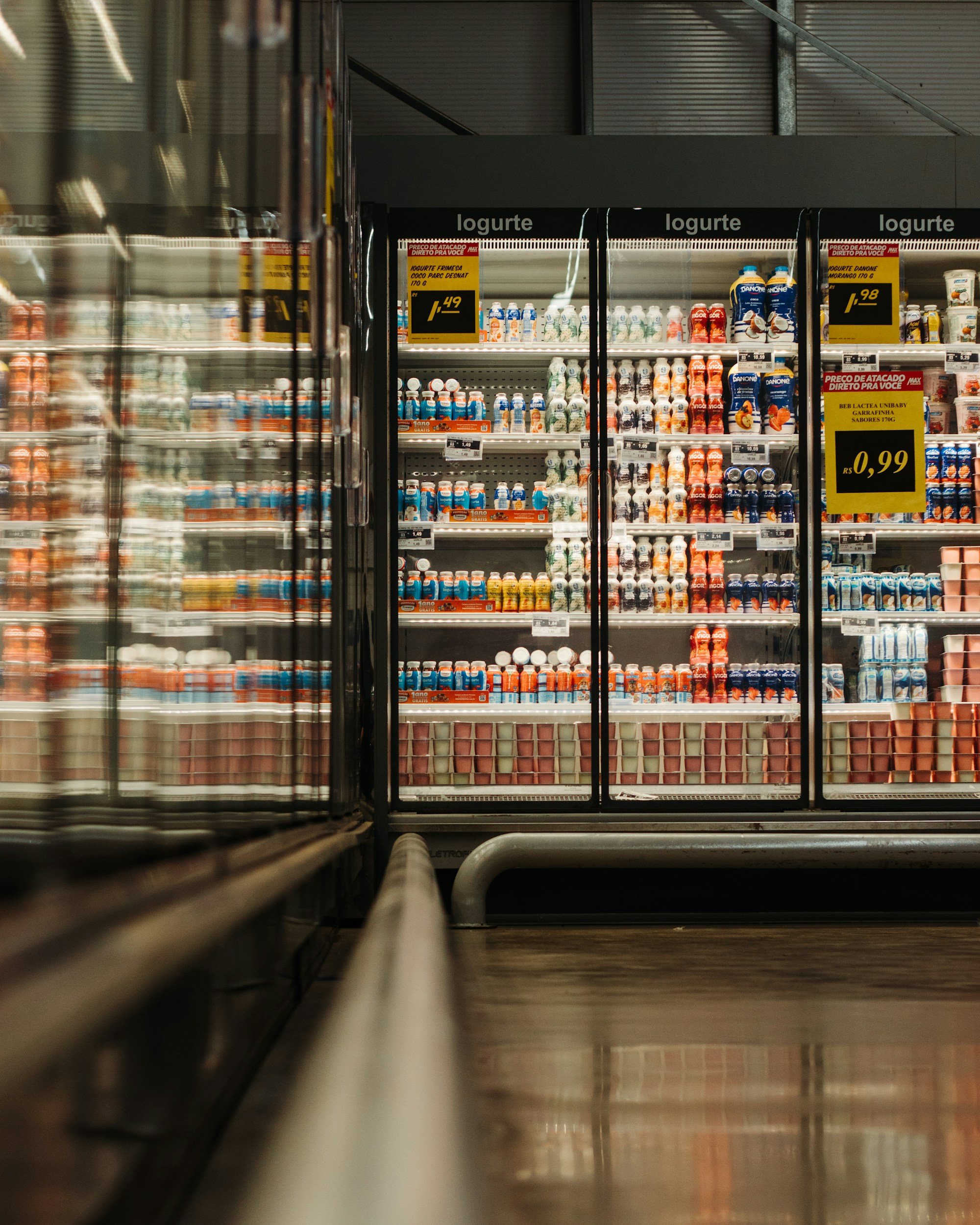 A refrigerated section in a store filled with various bottles and containers of dairy products, with prices displayed on yellow tags.