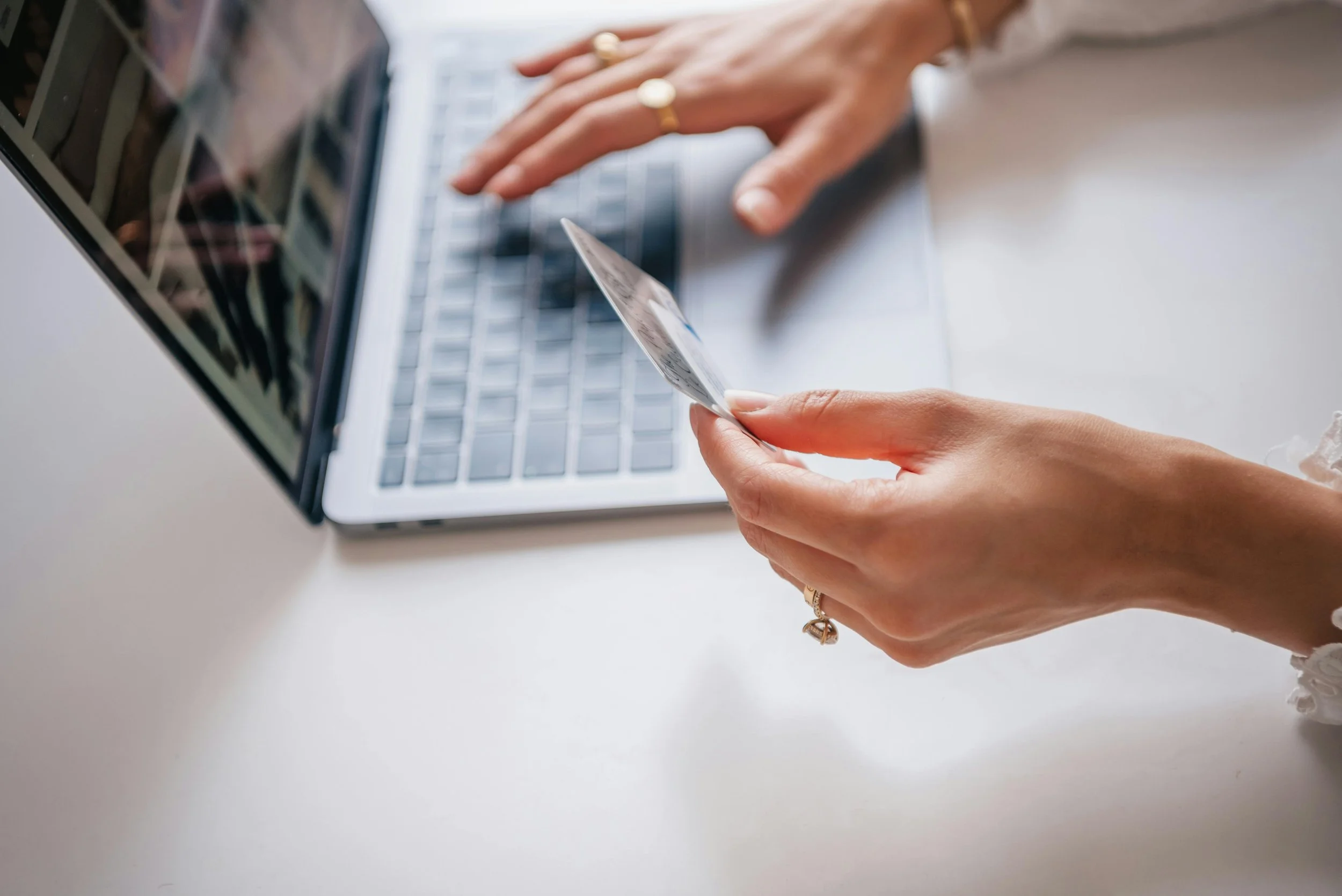 Close-up of a person holding a credit card in front of a laptop, possibly making an online purchase or payment.