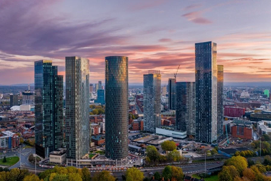 Skyline of modern skyscrapers at sunset in a city, with colorful sky and reflections on glass buildings.