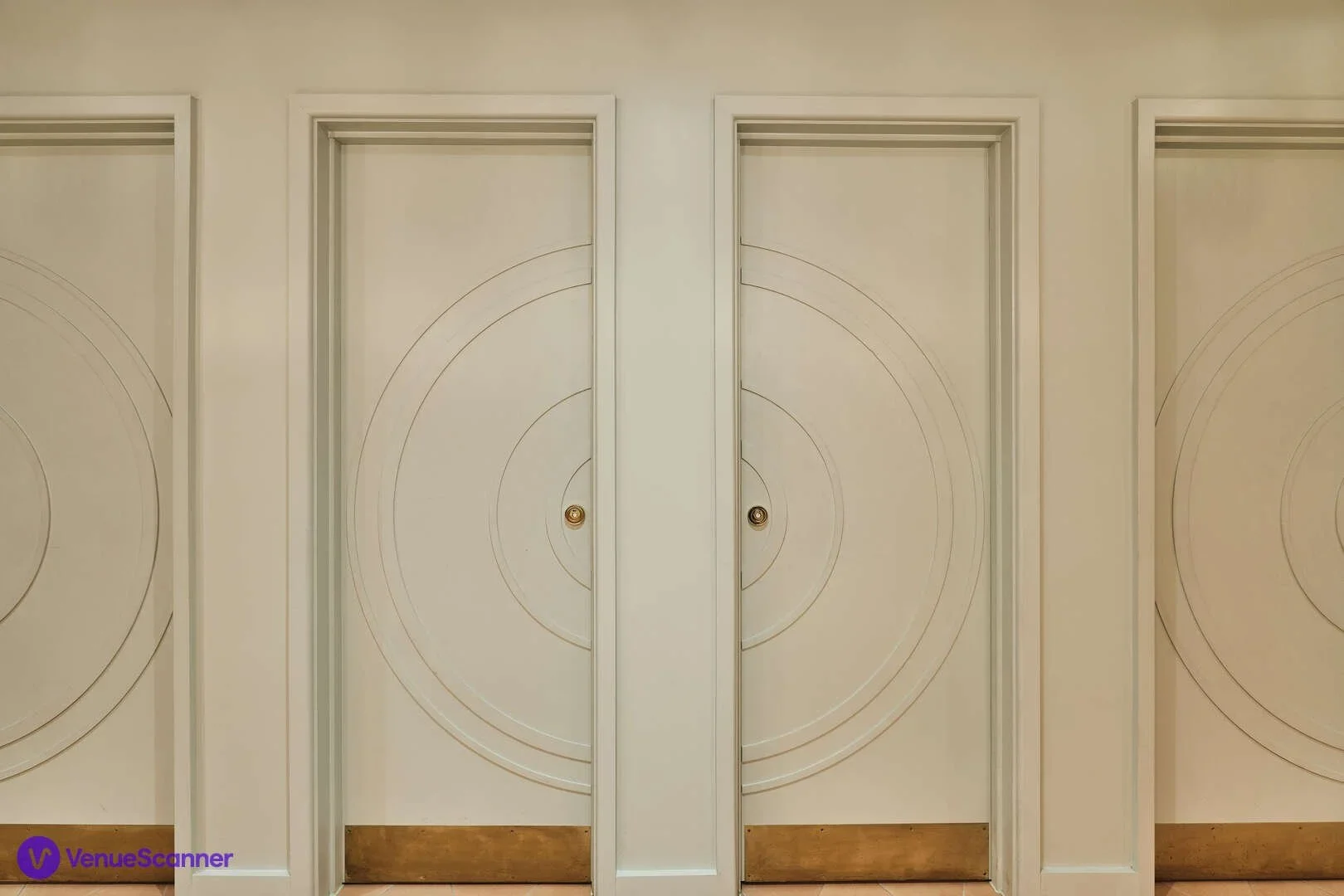 Two white doors with circular designs and gold handles, set within a white wall, with a wooden baseboard at the bottom.