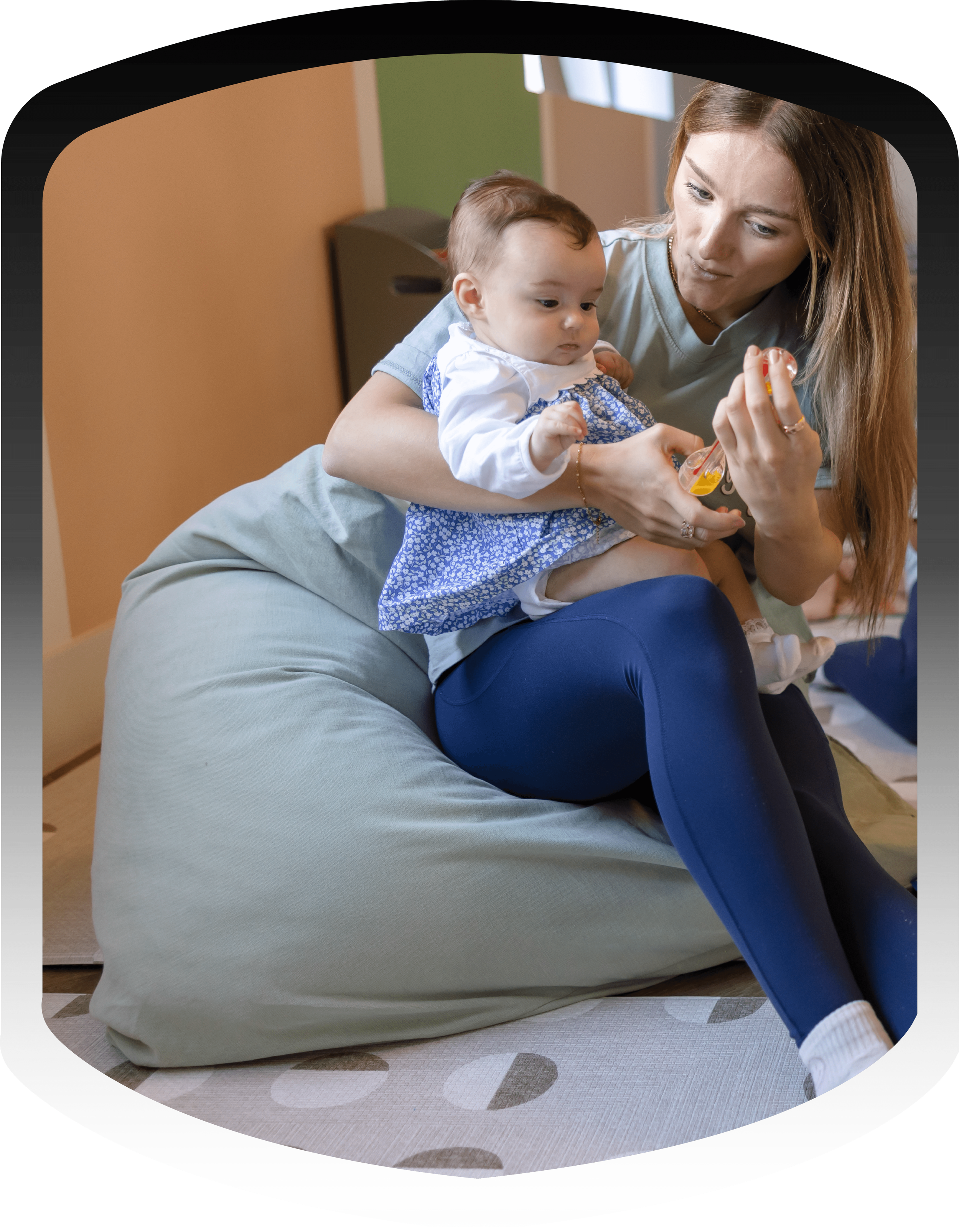 A woman sitting on a bean bag chair while holding a toddler girl and playing with a toy.