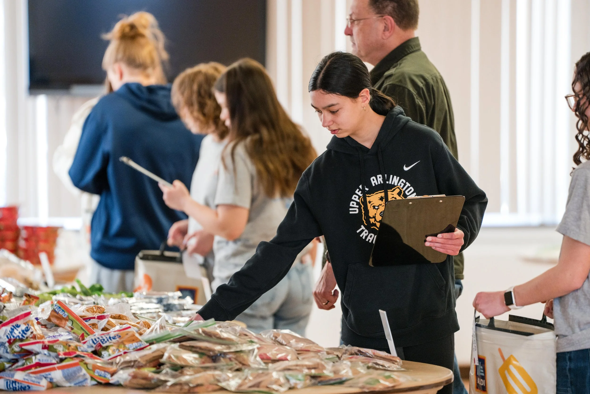 People shopping for food at a donation or charity event table containing various packaged foods.