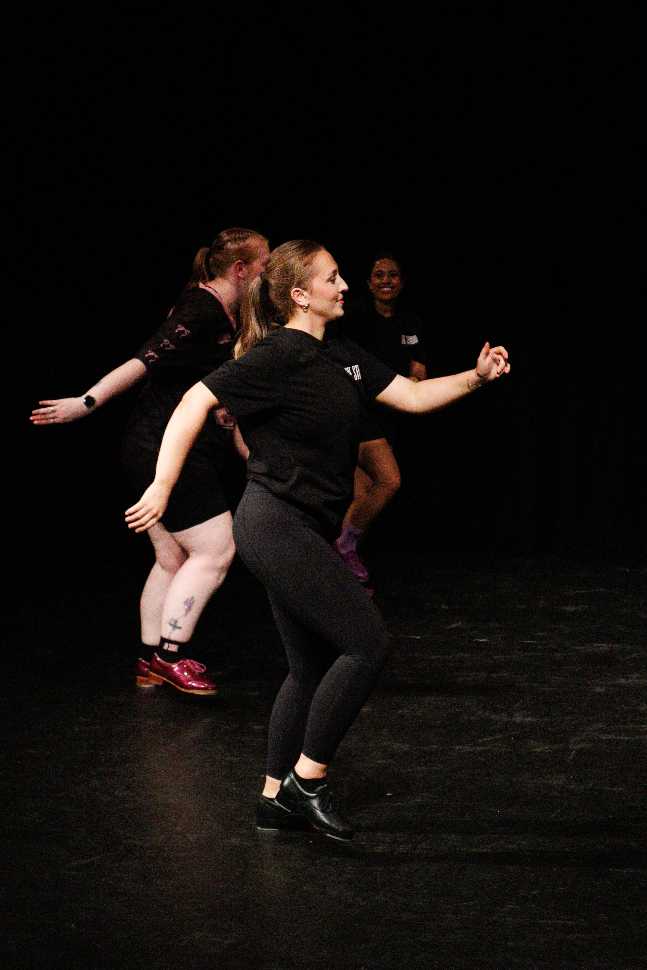 Four women dancing in a dark studio, smiling and having fun.
