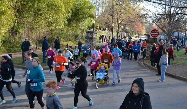 People participating in a community race or marathon outdoors in a park with trees and a pathway.