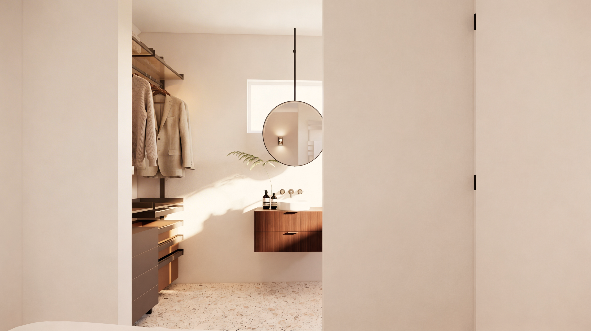 Een moderne inloopkast met beige en bruin houten opbergkasten en hangende kleding, een ronde spiegel en een wastafel met accessoires.