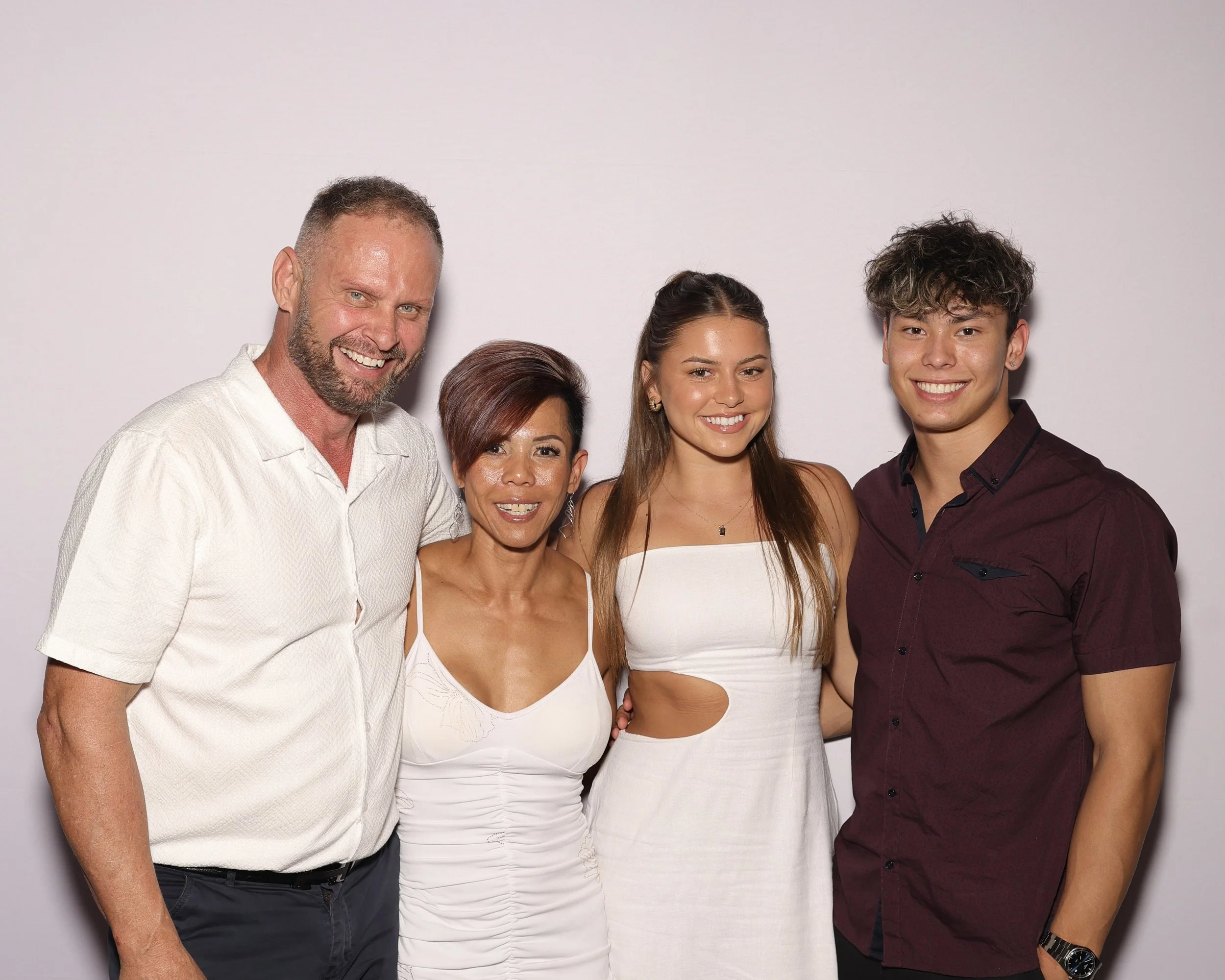 A group of five people standing close together and smiling in front of a white background.