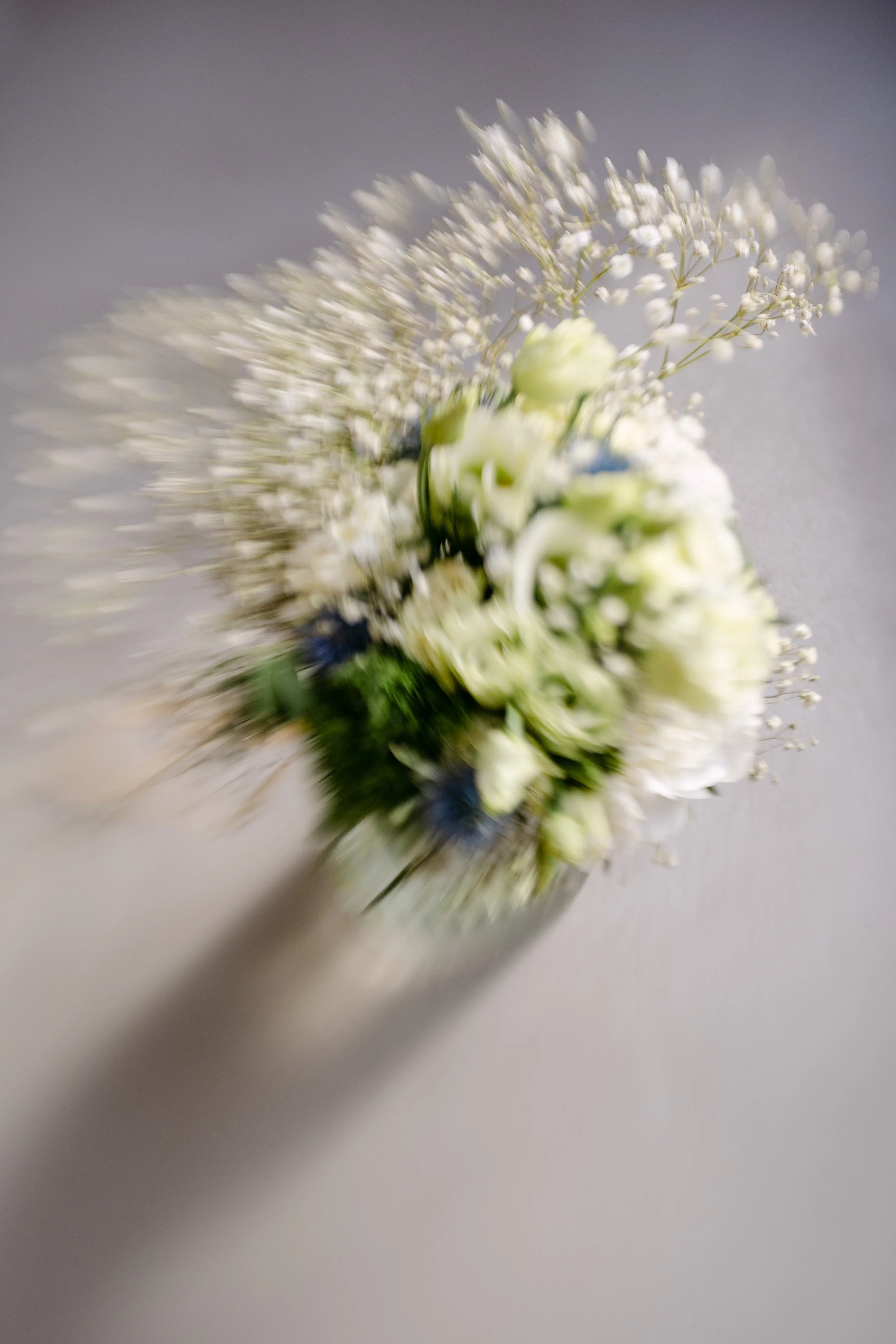 Blurred image of a bouquet of white flowers with some blue flowers and greenery.