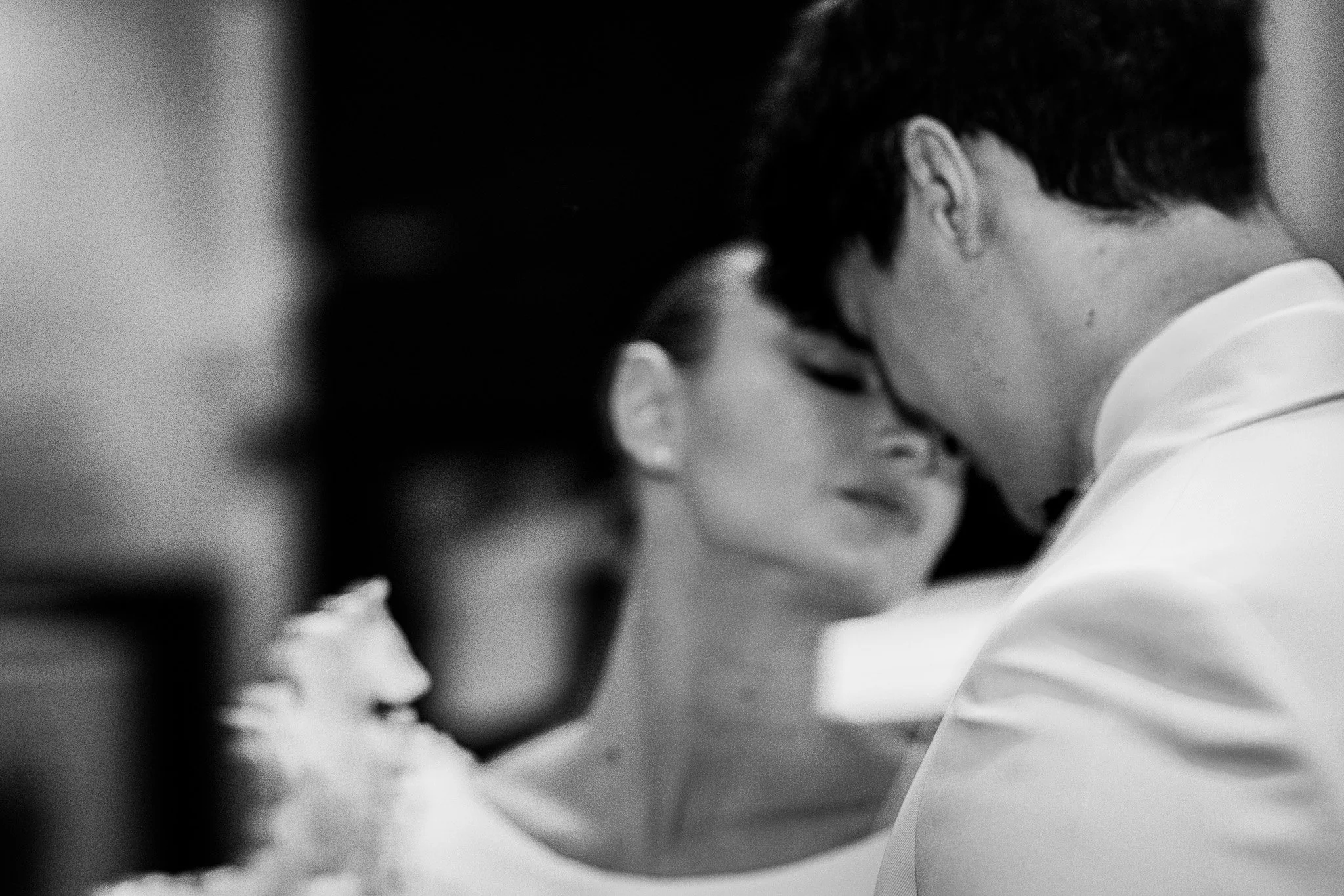A black and white close-up image of a young couple with eyes closed, touching foreheads and smiling softly.