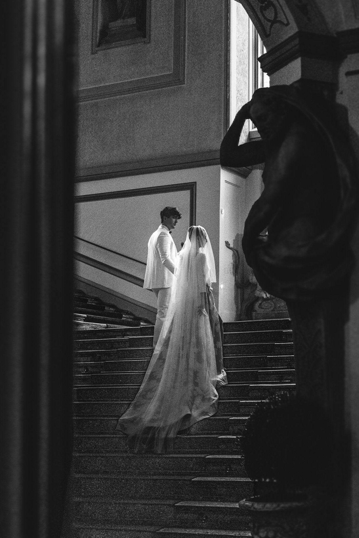 A wedding ceremony inside a building with stairs, showing a couple standing together by the window, and a dog in the foreground.