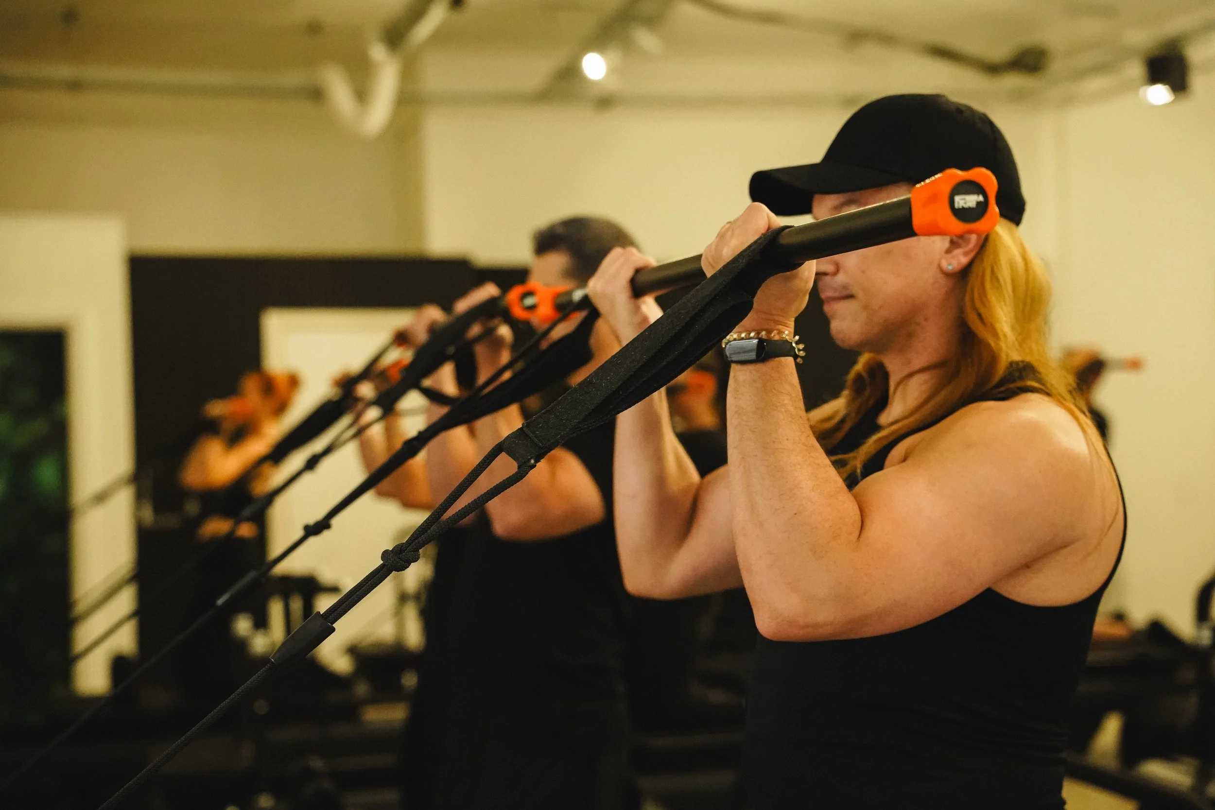 Women participating in a fitness class, holding resistance bars in front of their shoulders during an exercise.