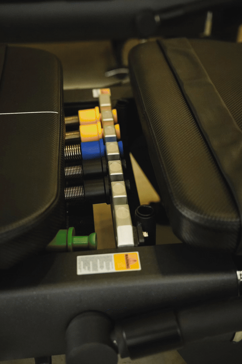 Close-up of a weight bench with dumbbells, colored weight plates, and a barbell, used for strength training exercises.