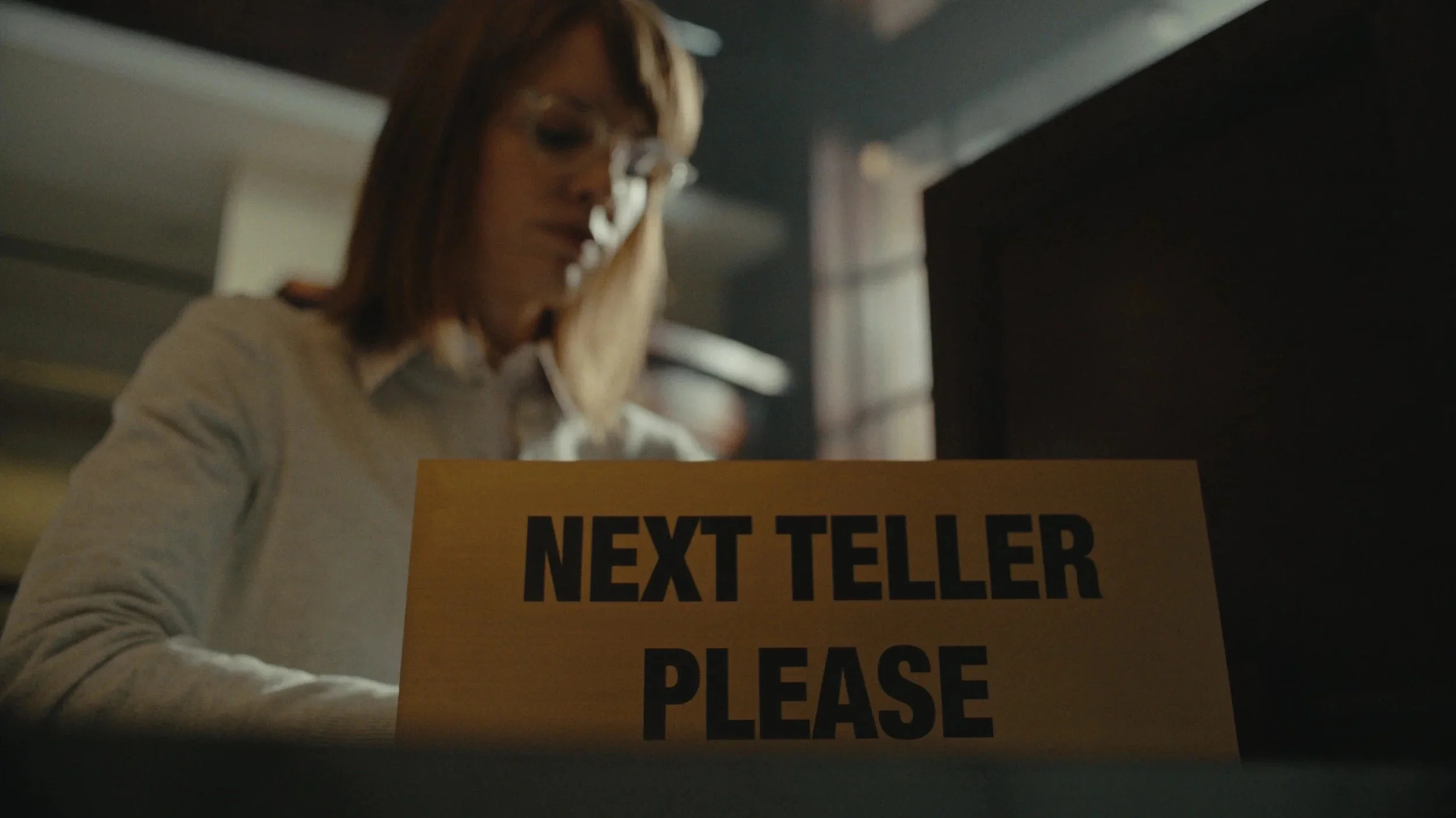 The “Next Teller Please” sign as a relic of outdated banking.